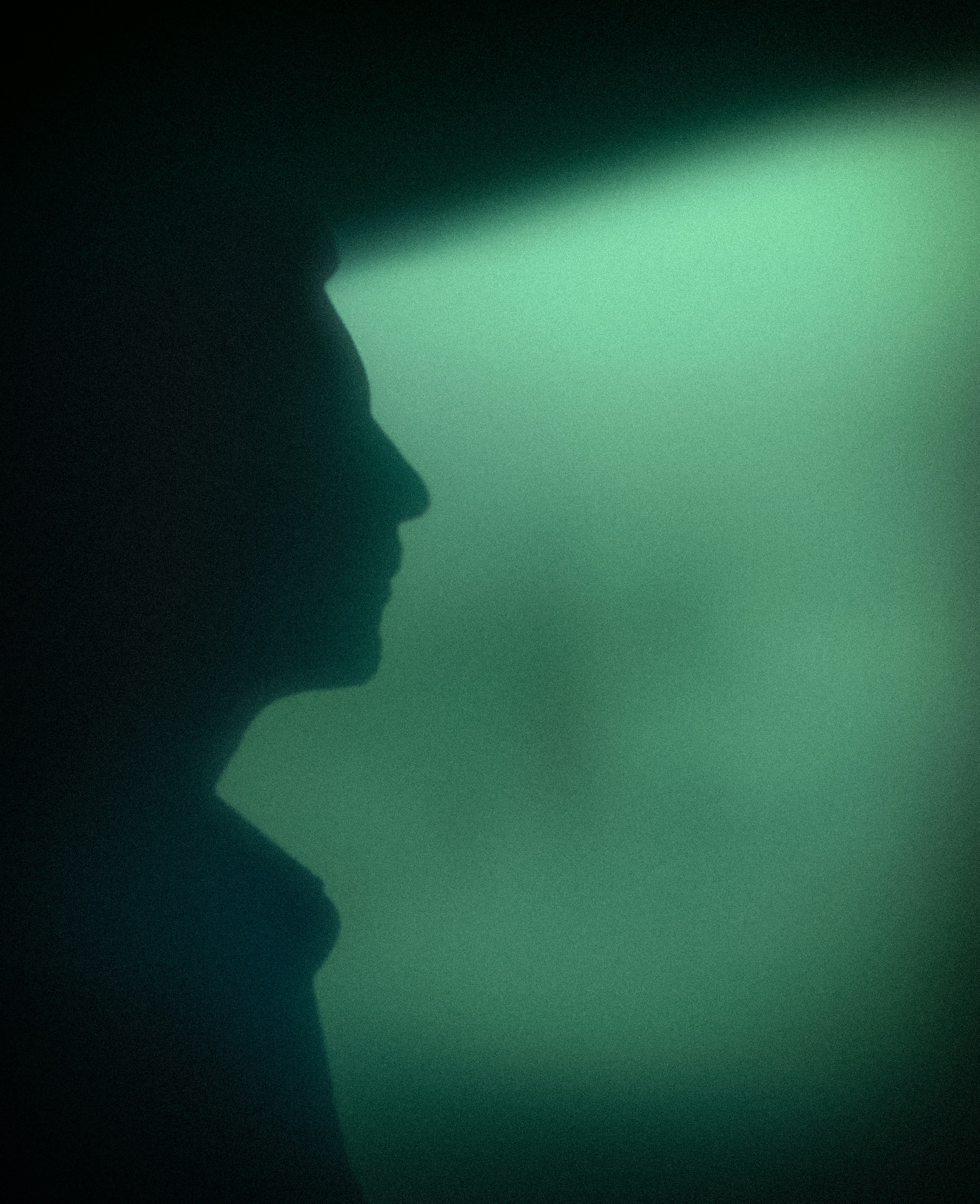 Silhouette of a person against a green, textured wall.