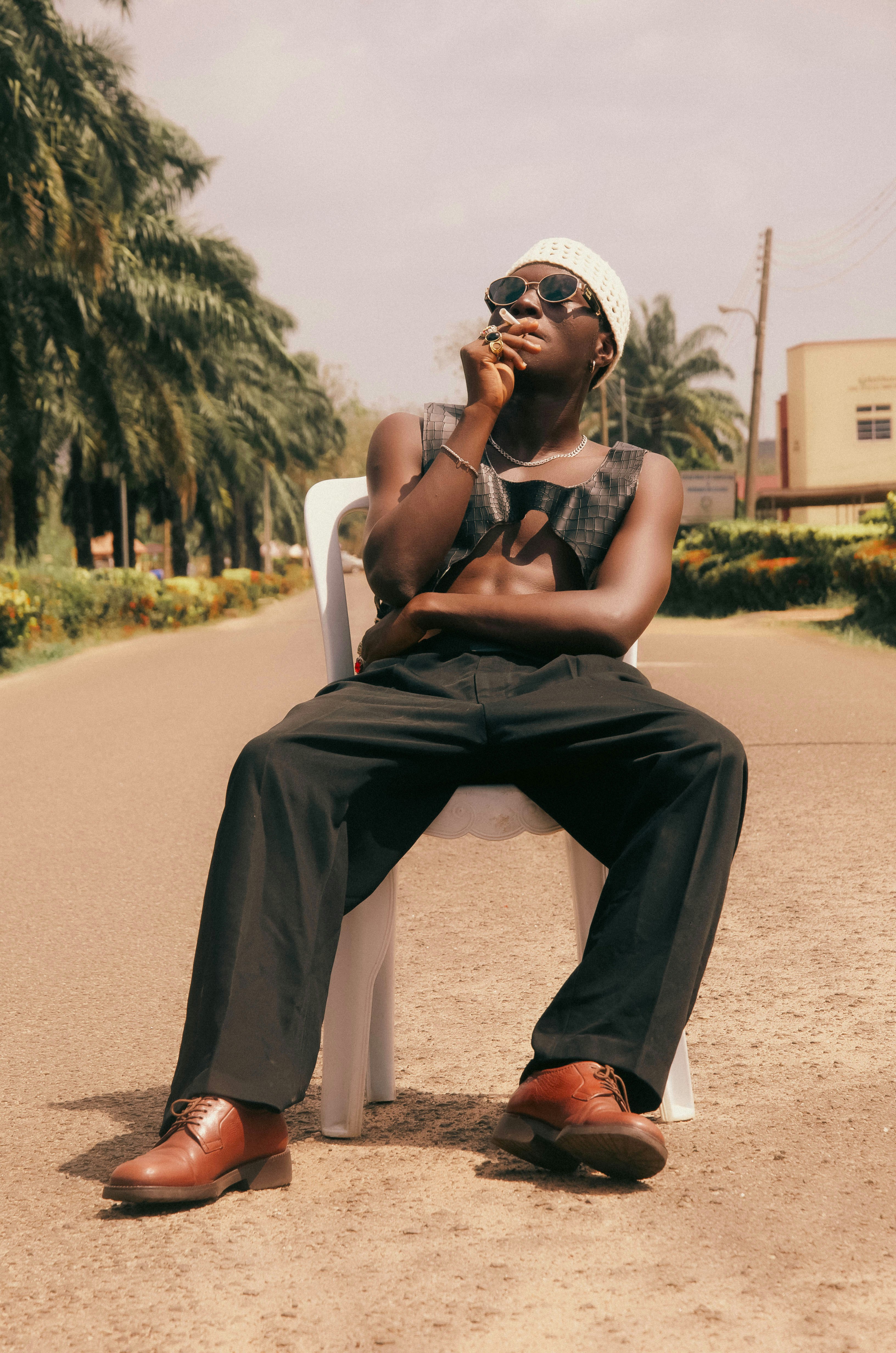 Man in sunglasses and hat smoking on a chair.