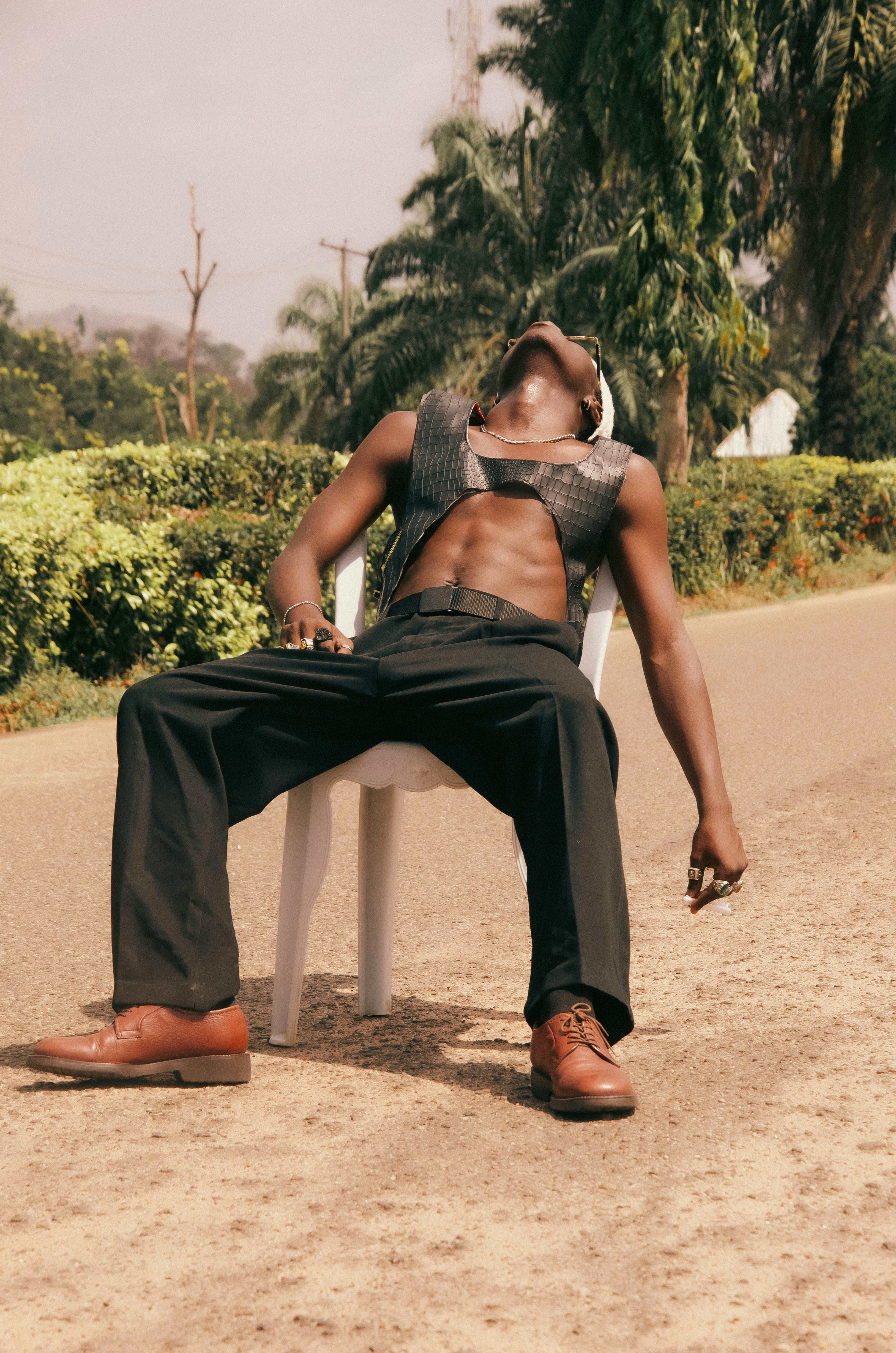 Man in leather vest and black pants sits outdoors.