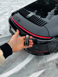 Hand holding car key in front of black porsche