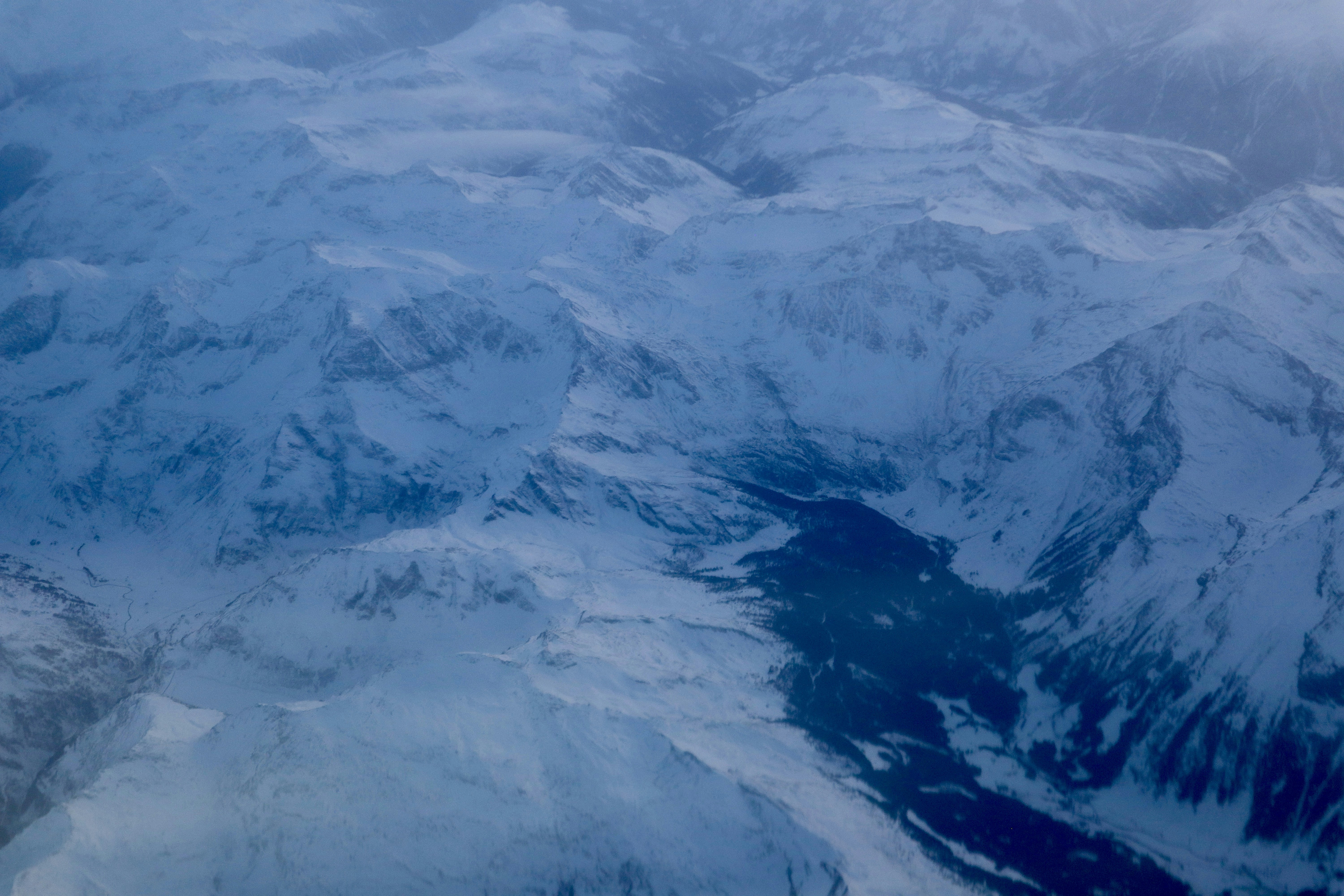 Snow covered mountains with a dark valley below.