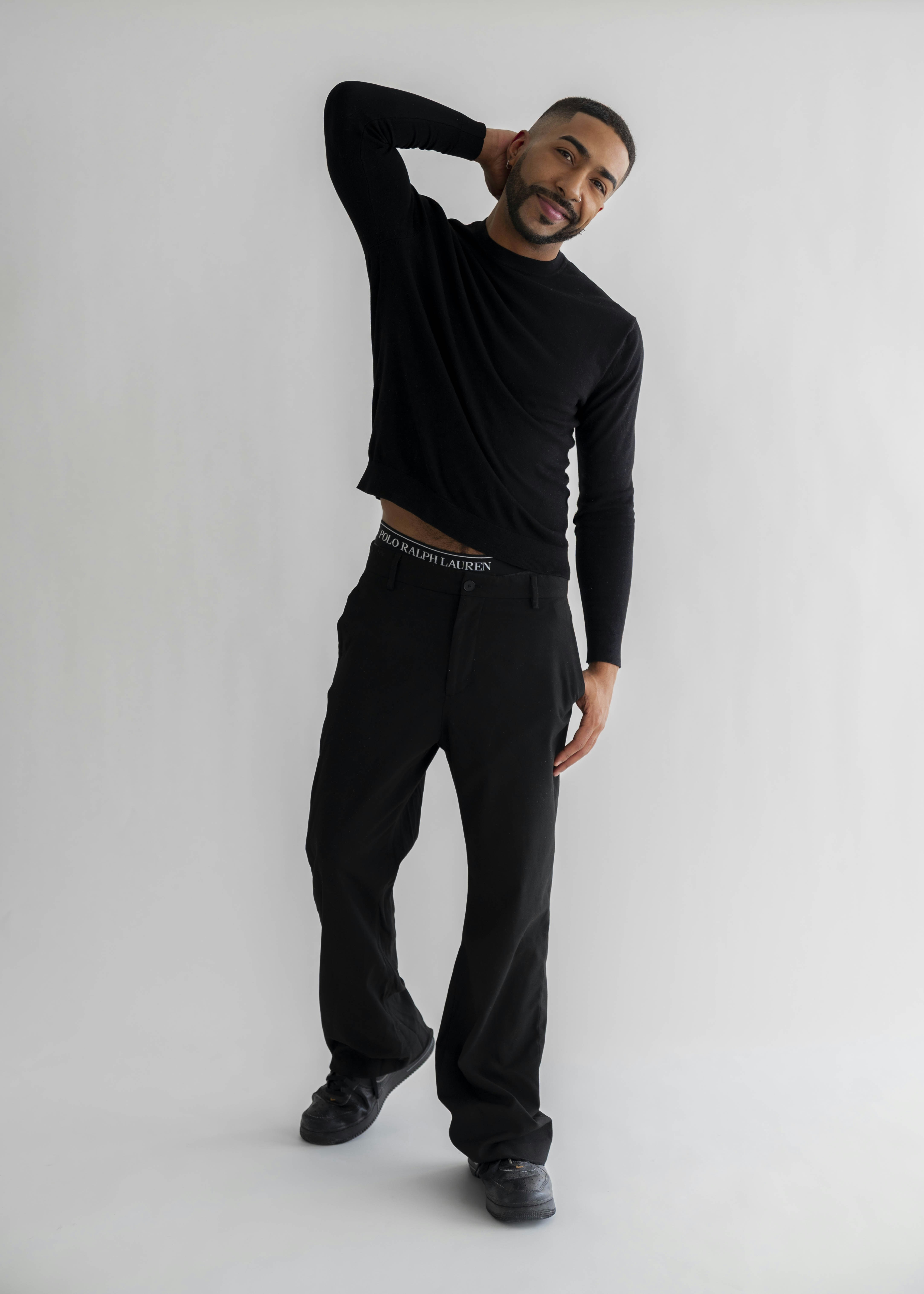 A man in black clothing poses against a white background