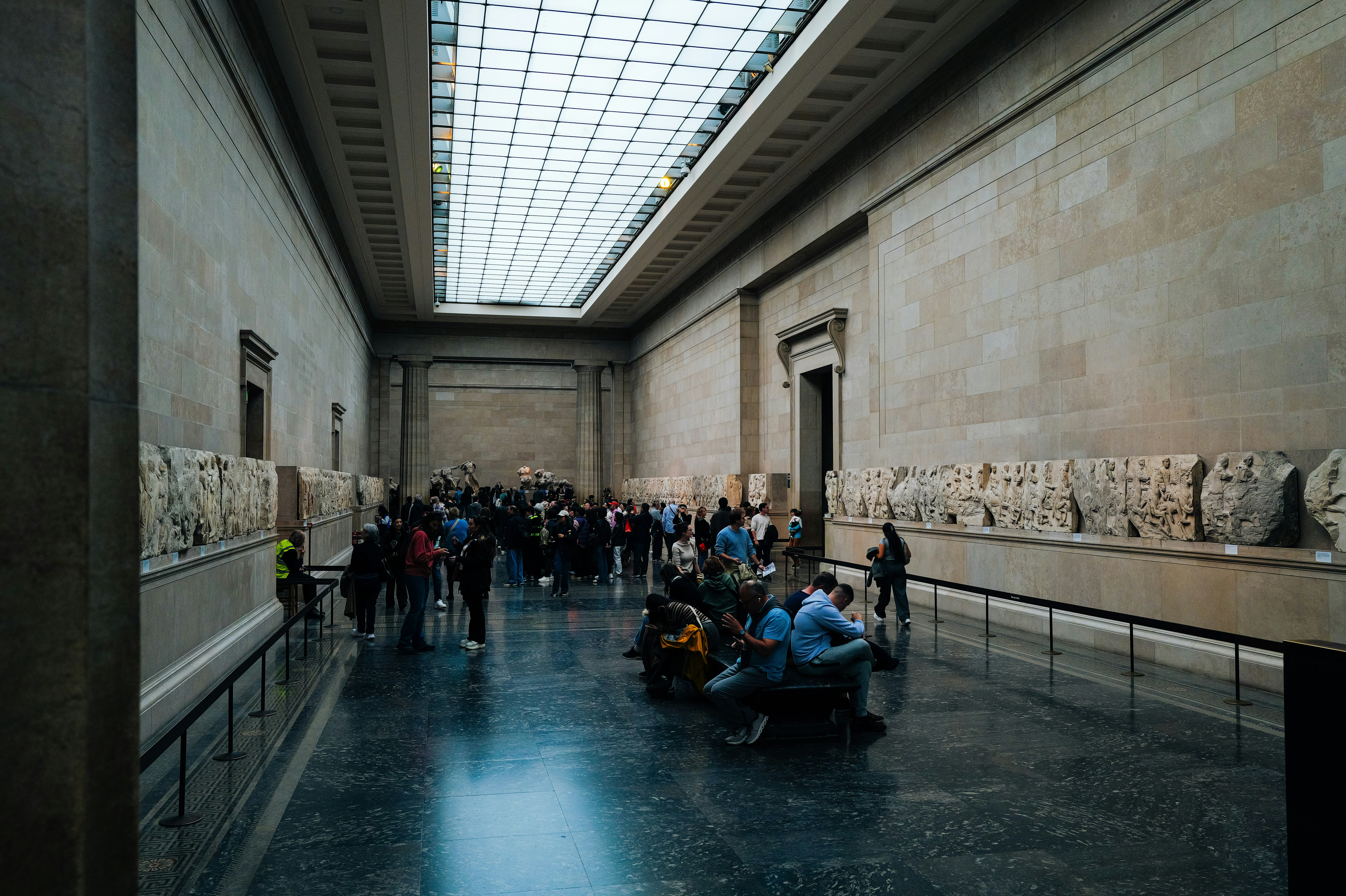웅장한 박물관 홀에서 조각을 감상하는 사람들.