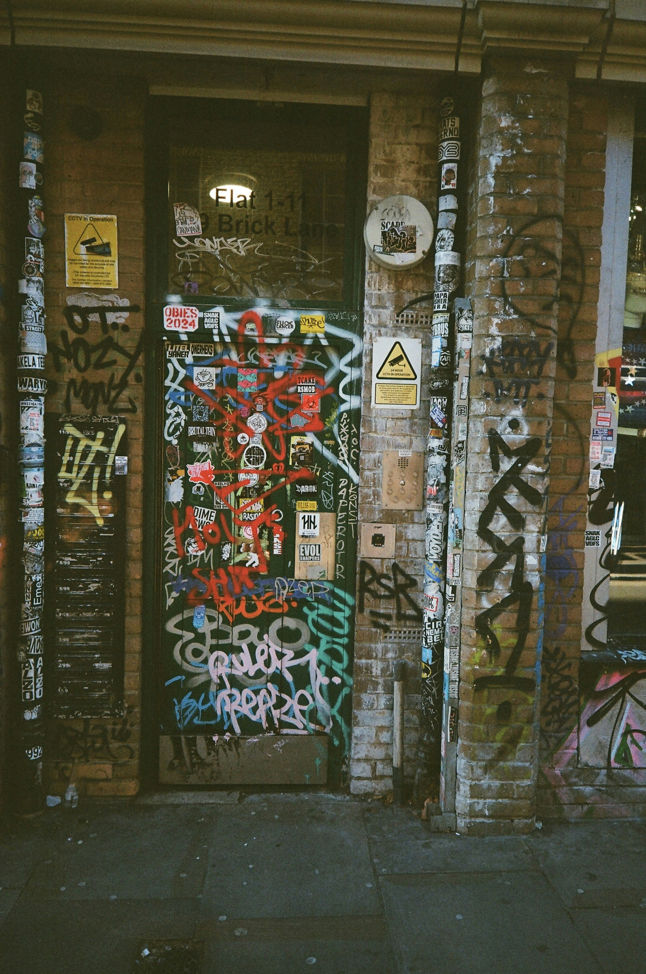 A graffiti-covered door and brick wall on a street.