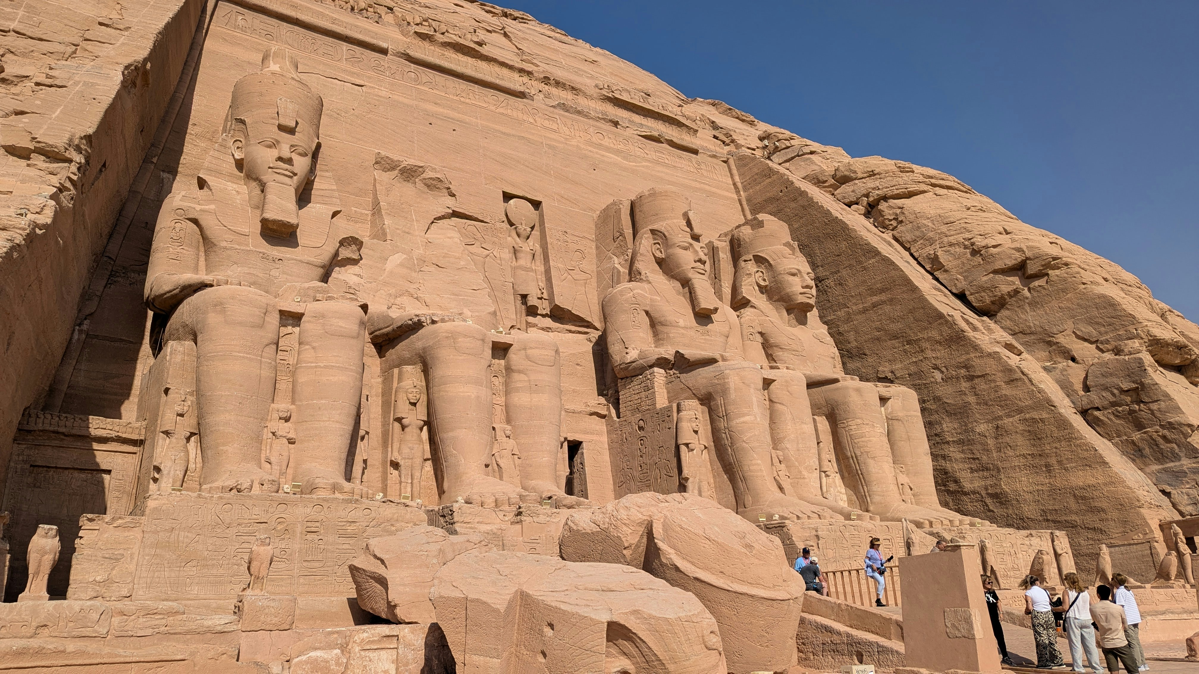 Massive ancient statues carved into a sandy cliff face.