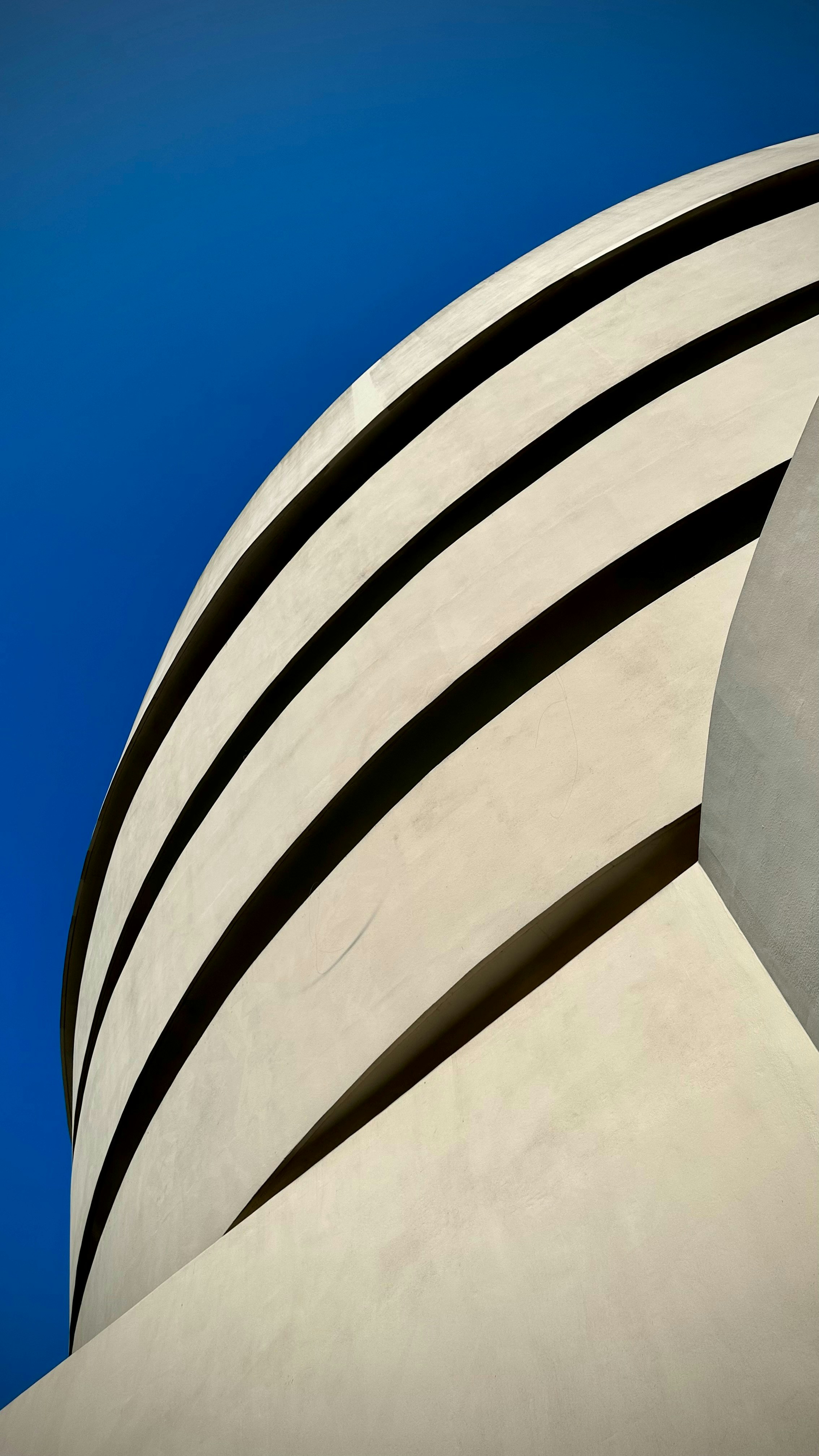 Curved white building with black stripes against blue sky.