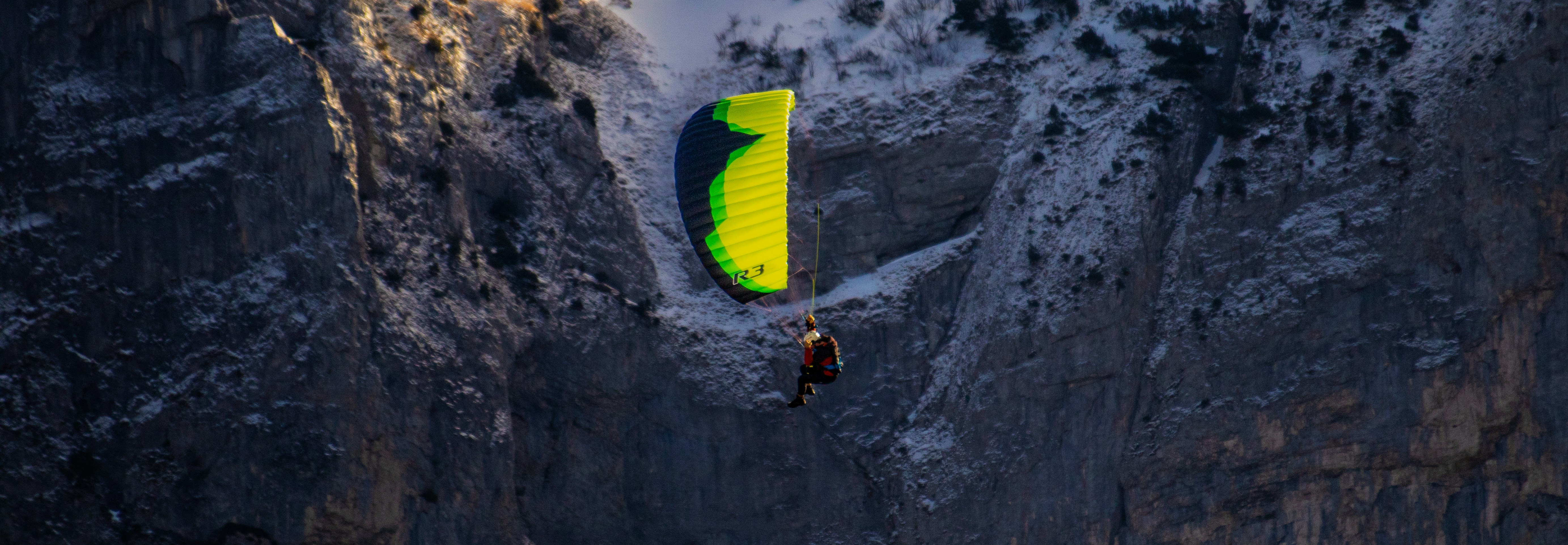 Paraglider soars against a rocky mountain backdrop
