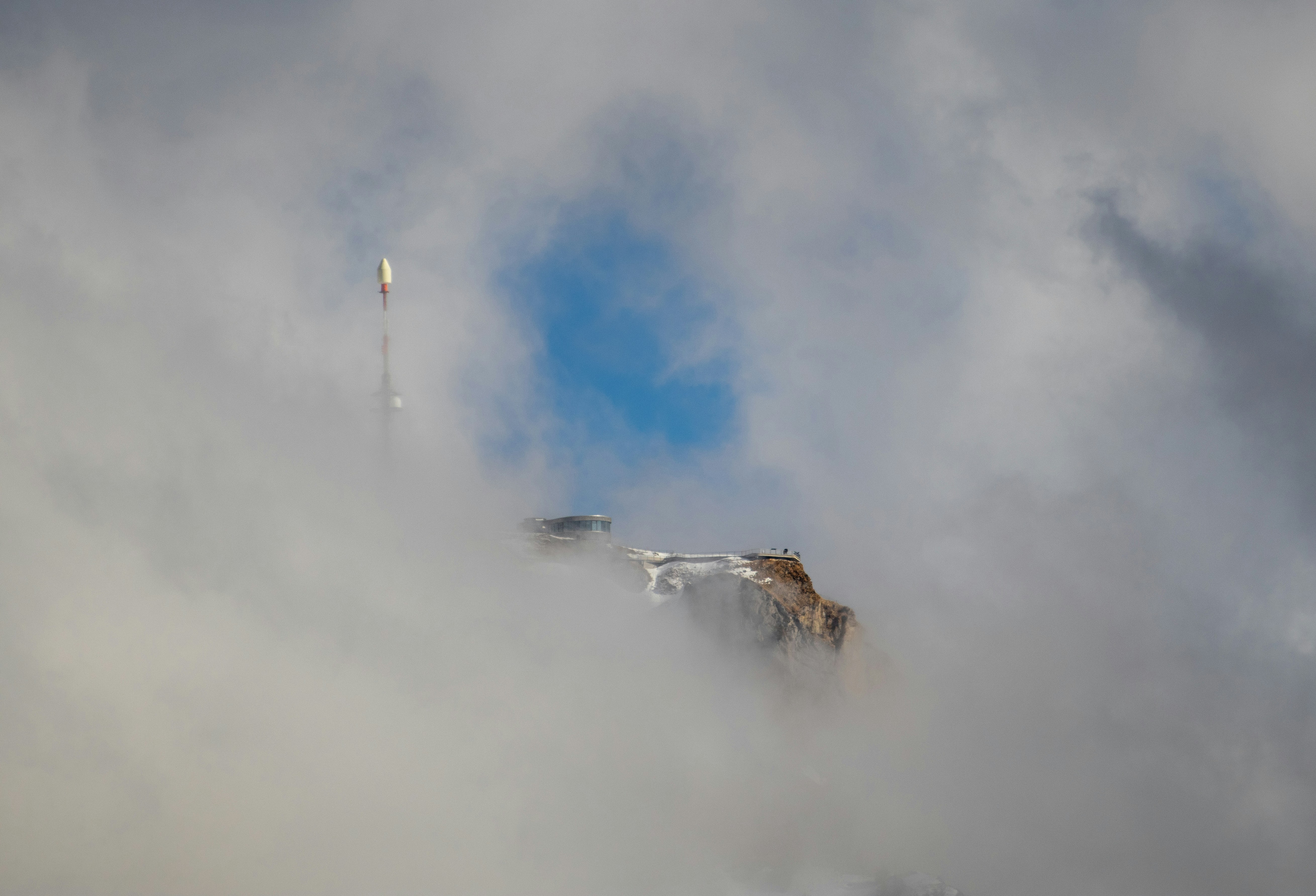 A building emerges from thick clouds with blue sky above.