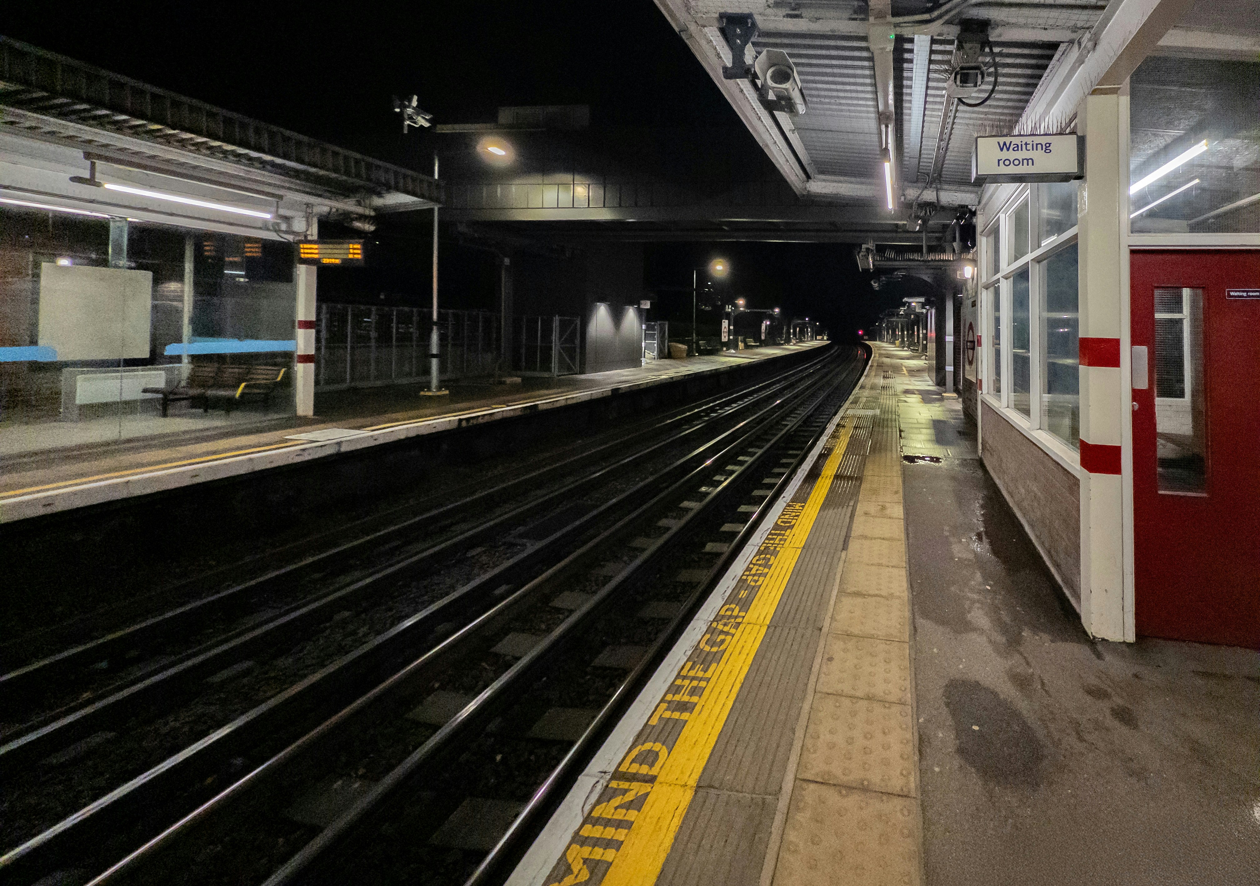 Empty train station platform at night with wet tracks.