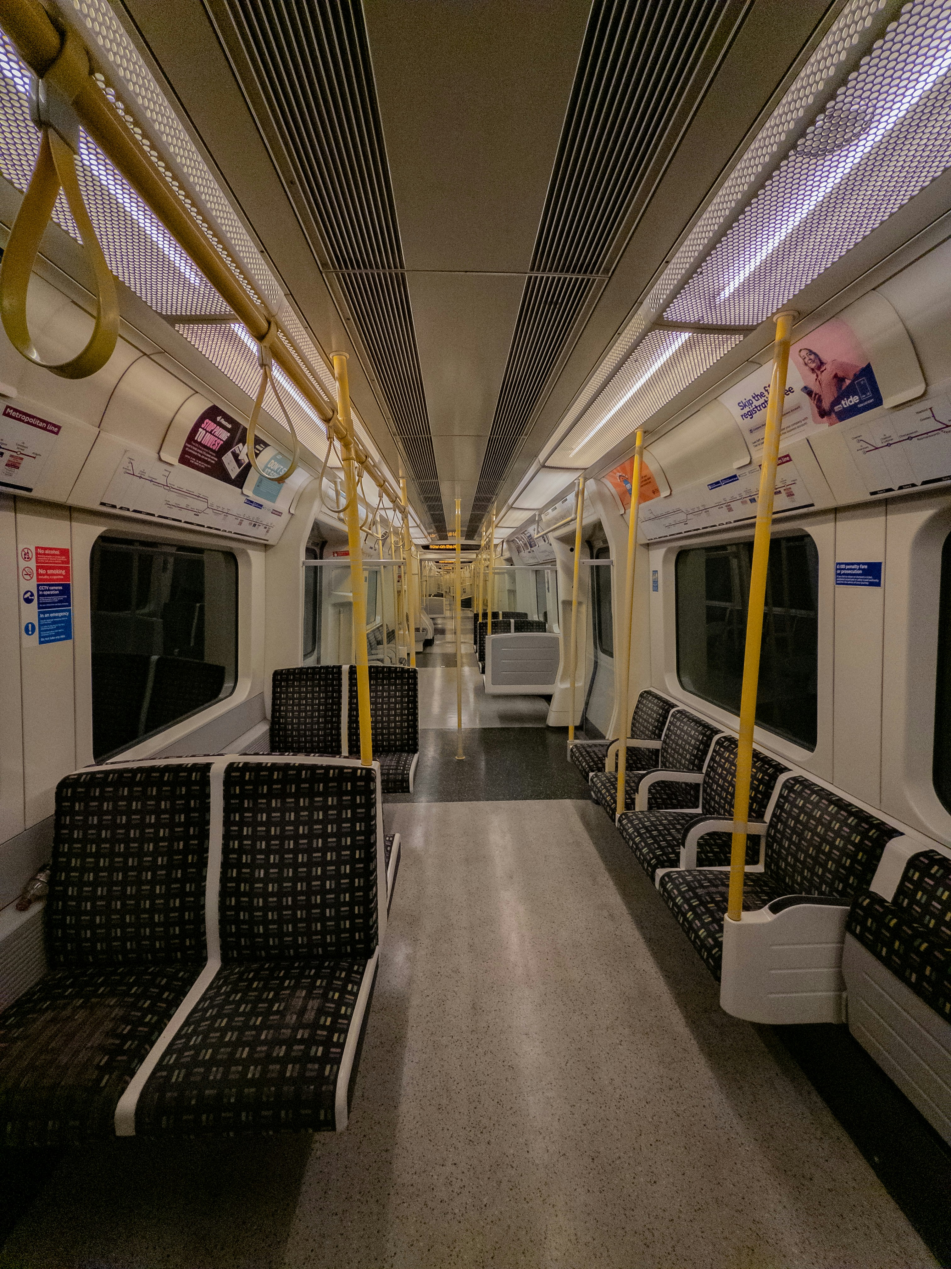 Empty train carriage with patterned seats and yellow poles.