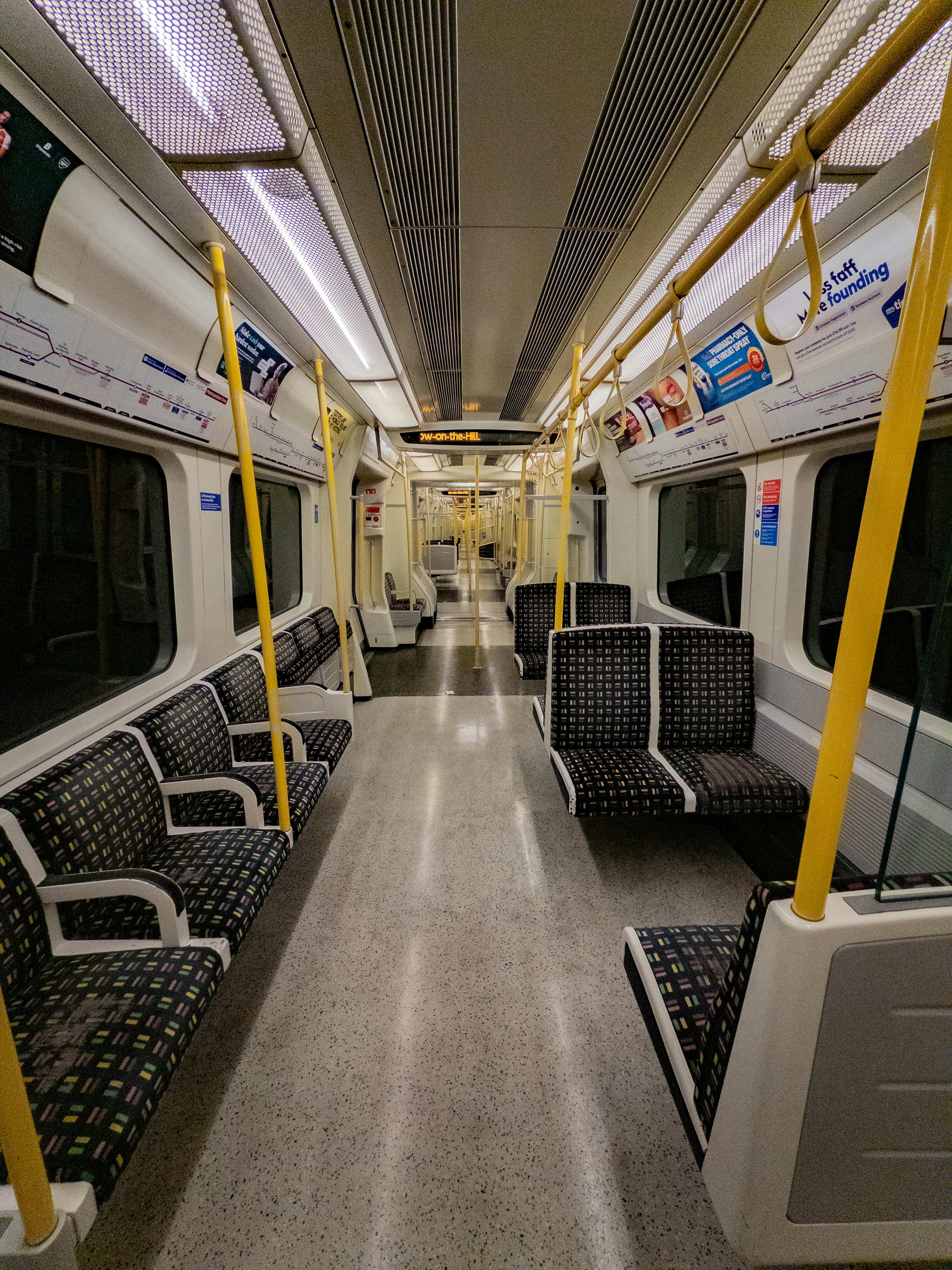 Empty subway train interior with patterned seats and yellow poles.