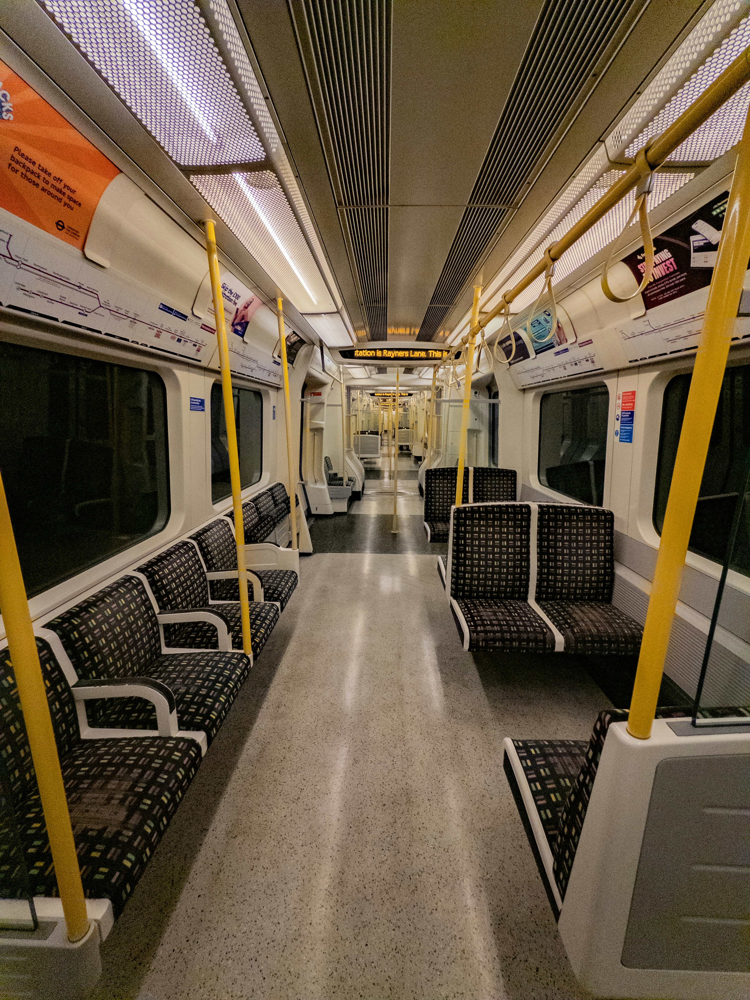 Empty subway train interior with patterned seats and yellow poles.