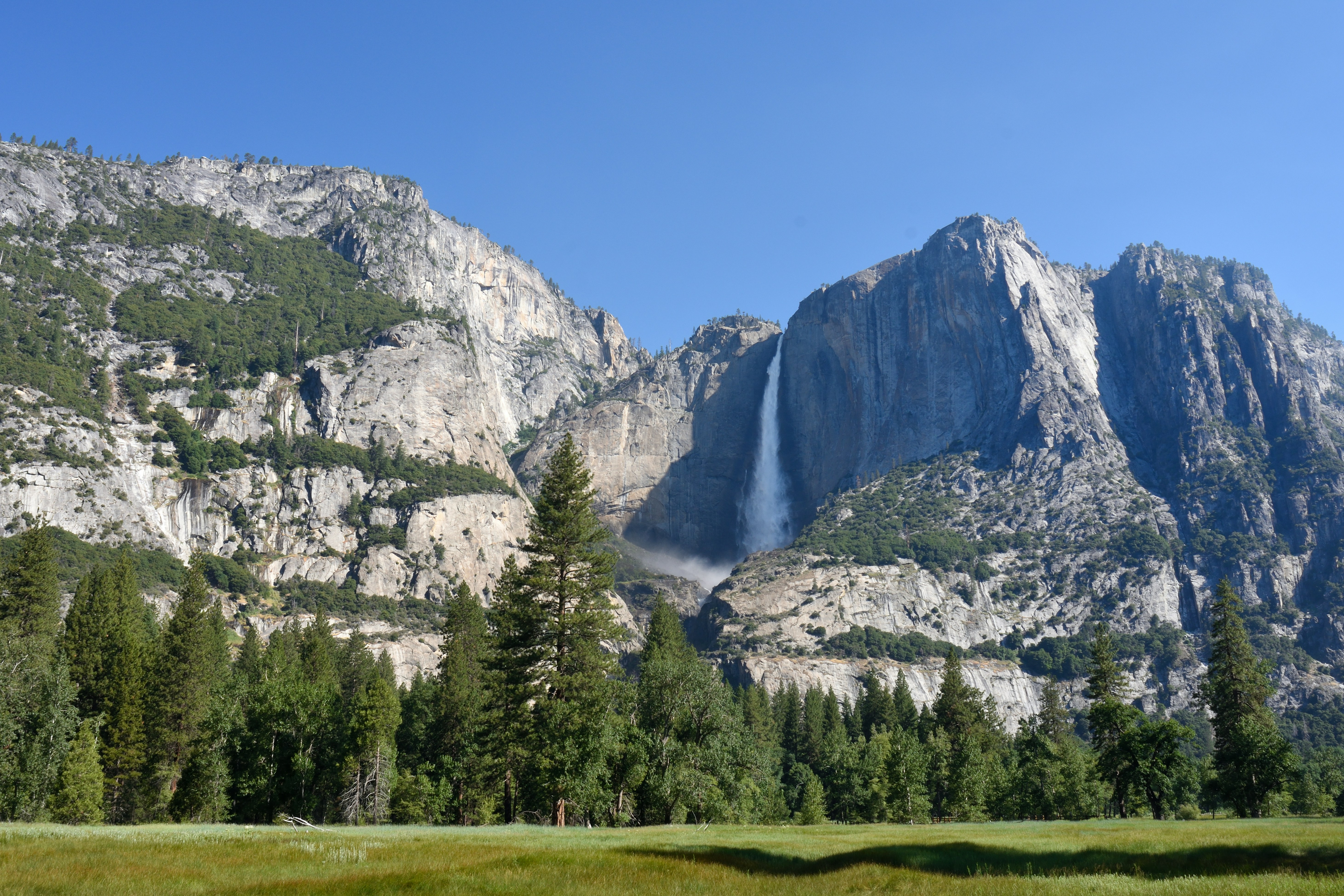 Waterfall cascading down a rocky mountain face with green trees.