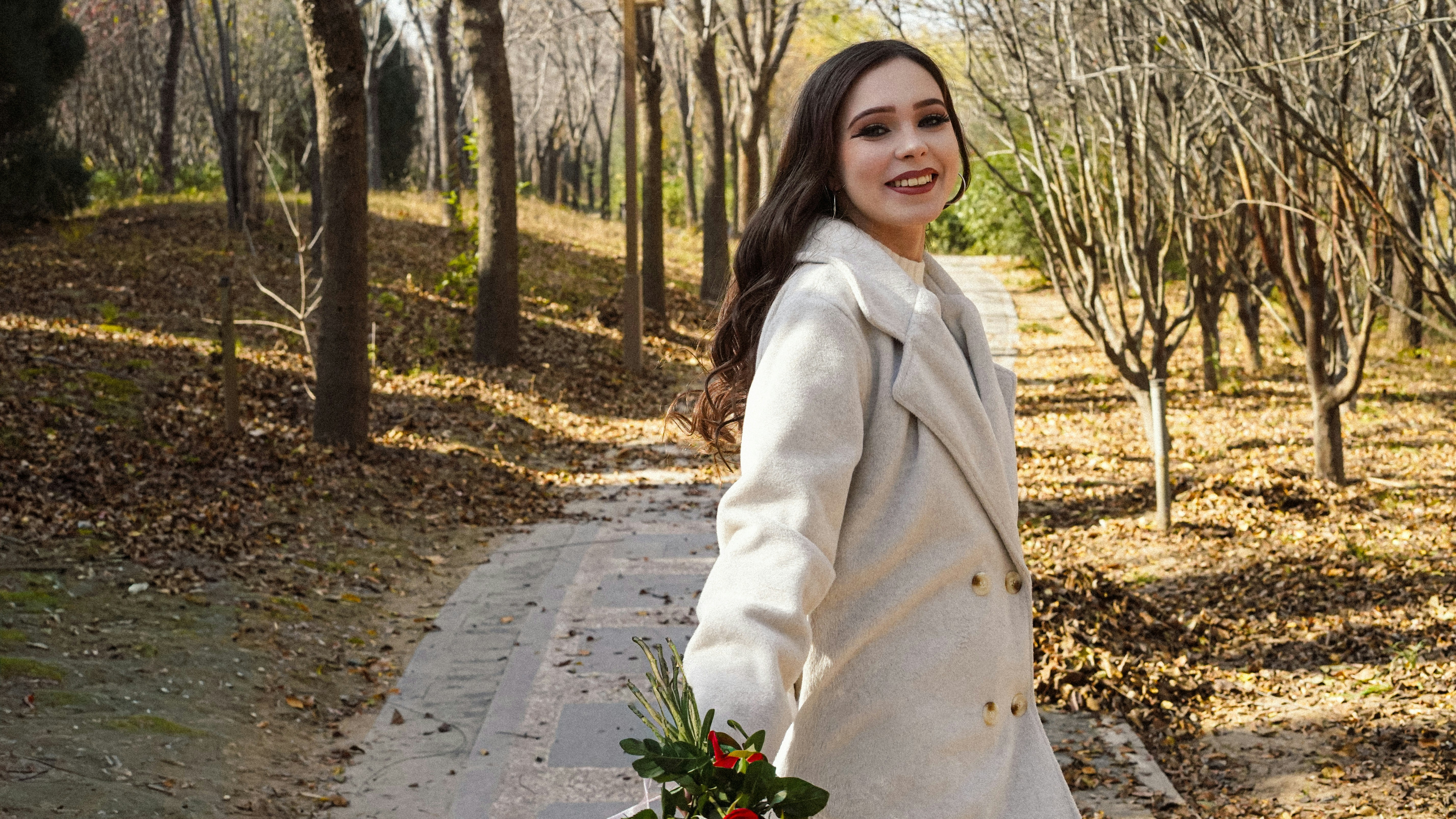 Young woman walking in autumn park with bouquet.