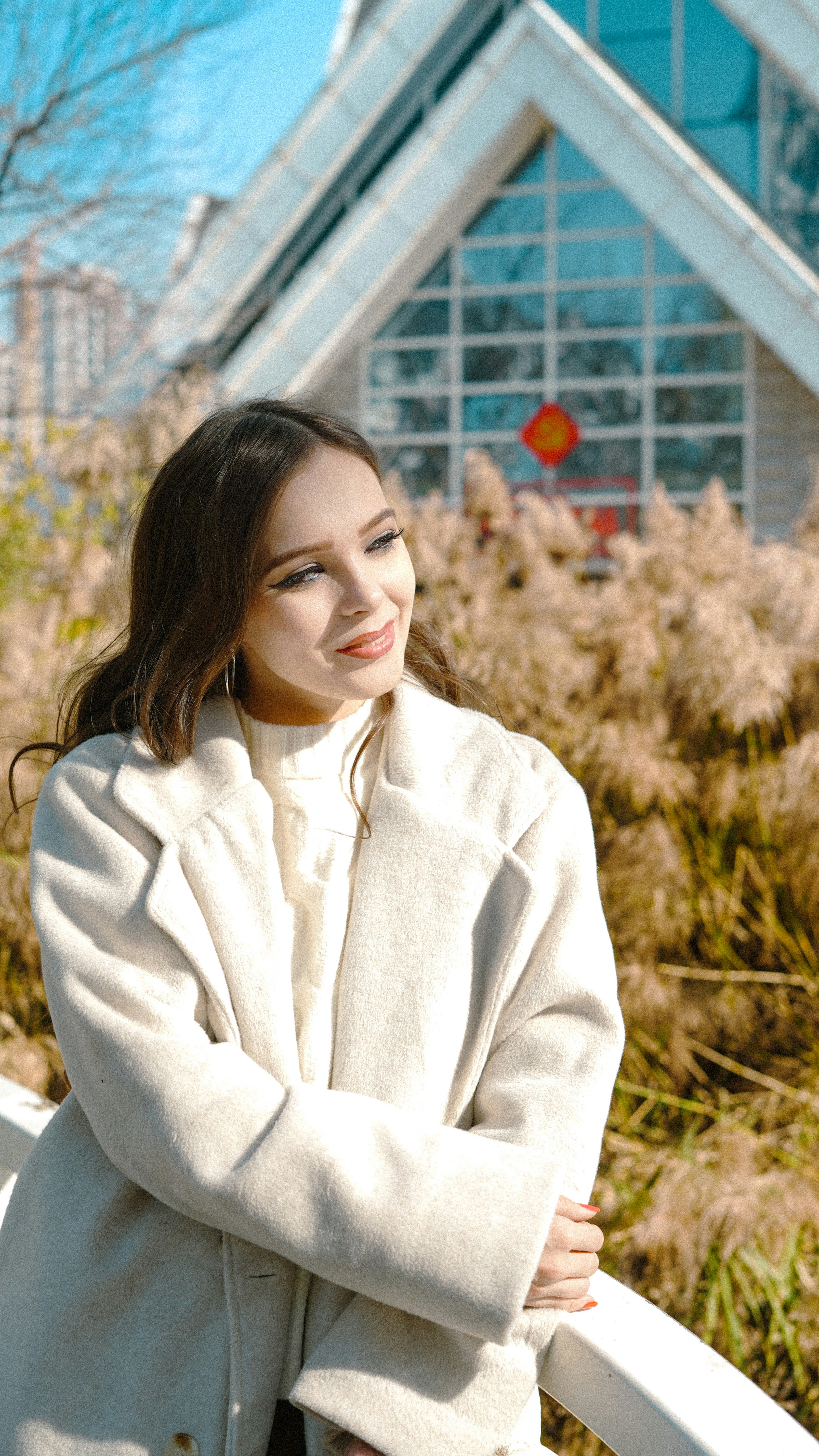 Young woman in a white coat standing near tall grass.