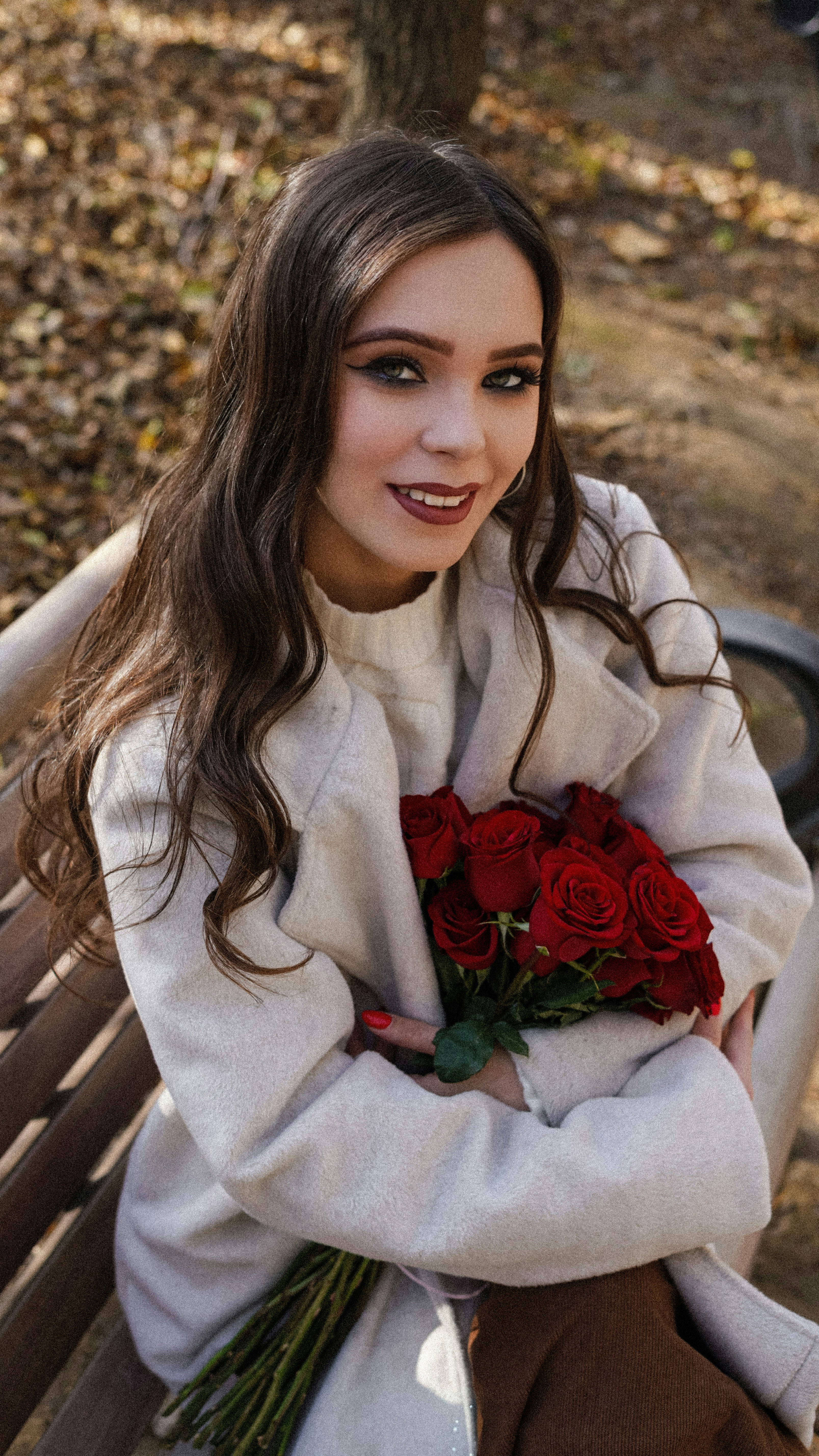 Young woman with bouquet of red roses sitting on bench