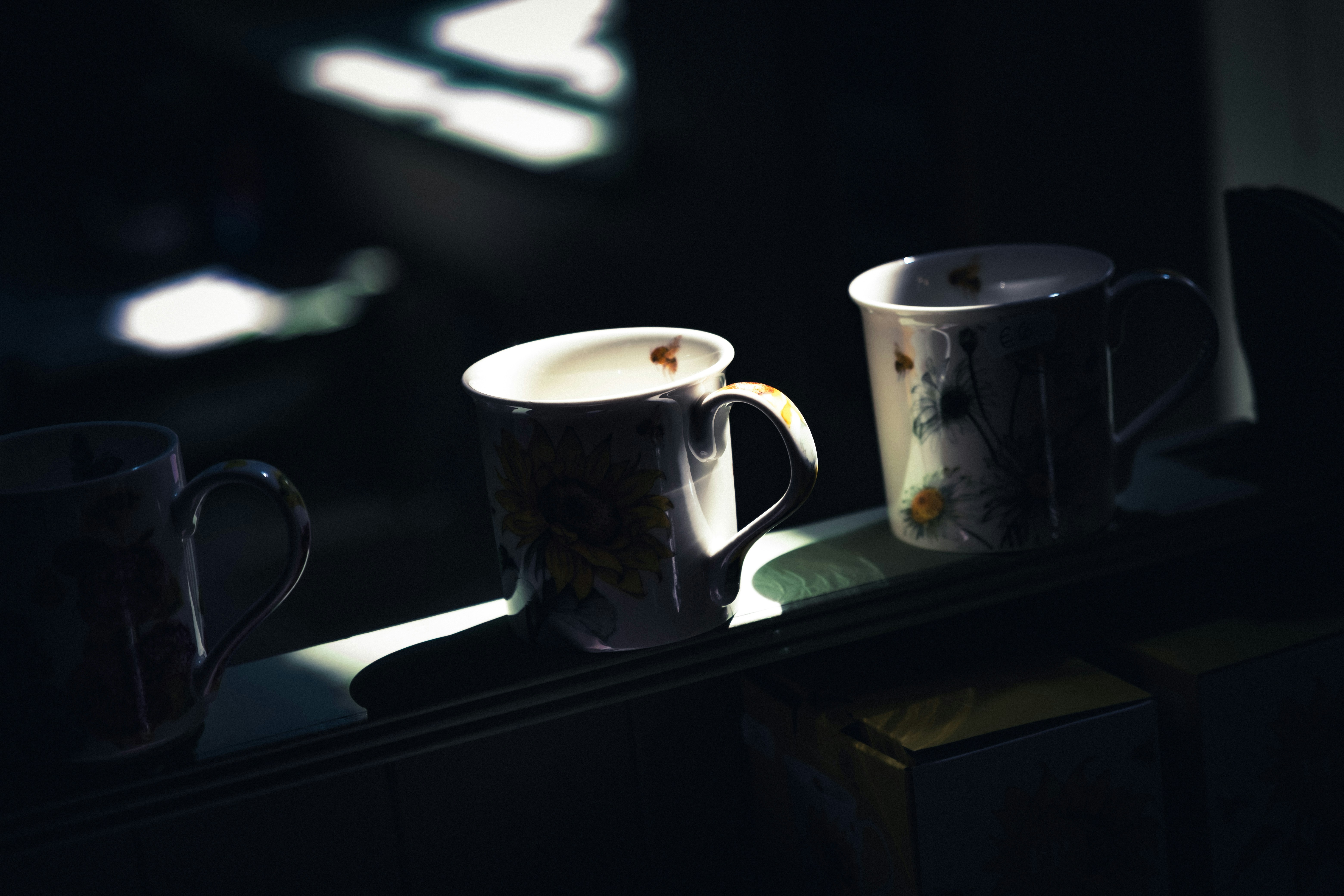 Drei Tassen stehen im gesprenkelten Sonnenlicht auf einem Regal.