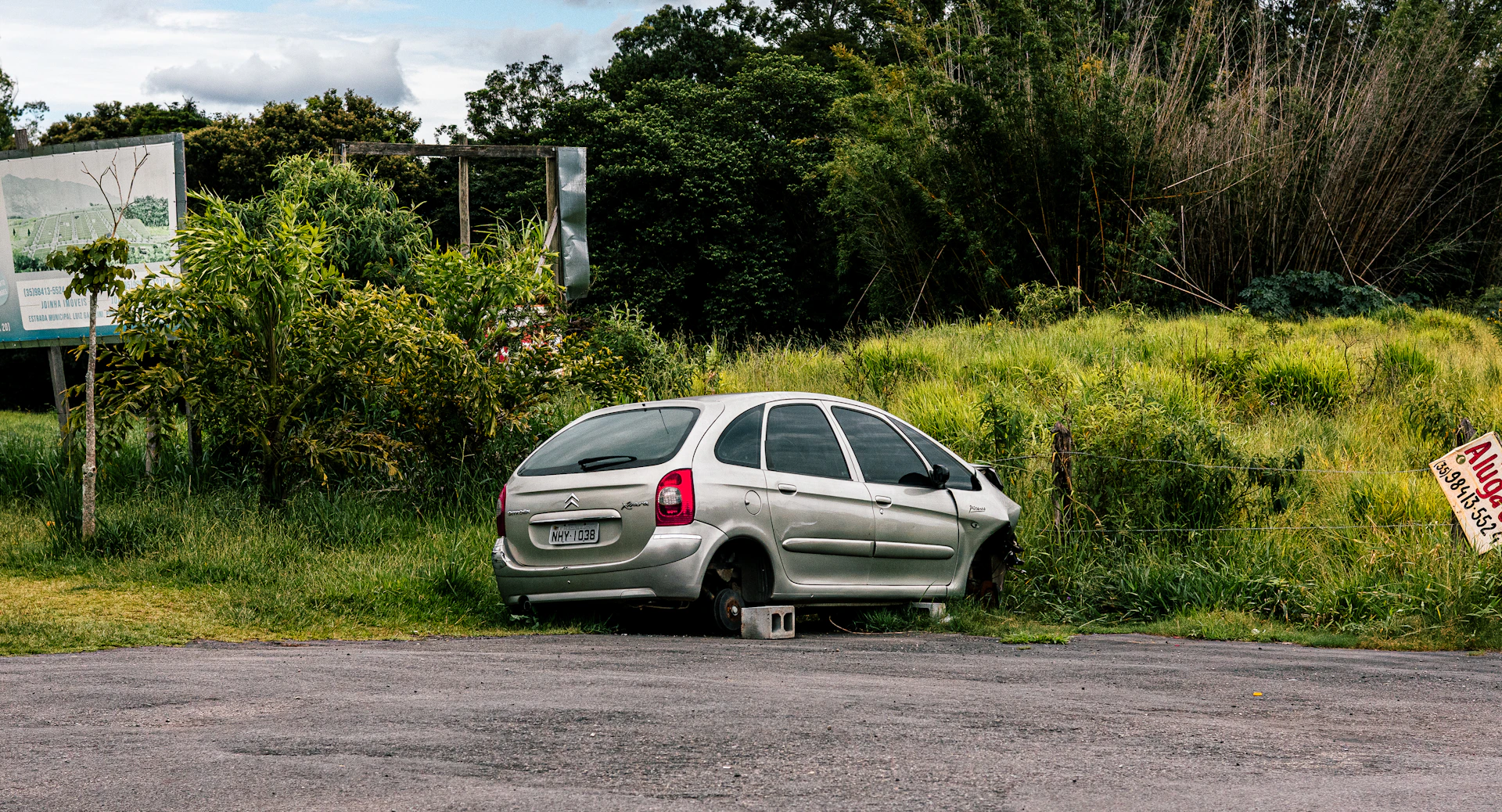 Silver car with missing wheel in overgrown grass