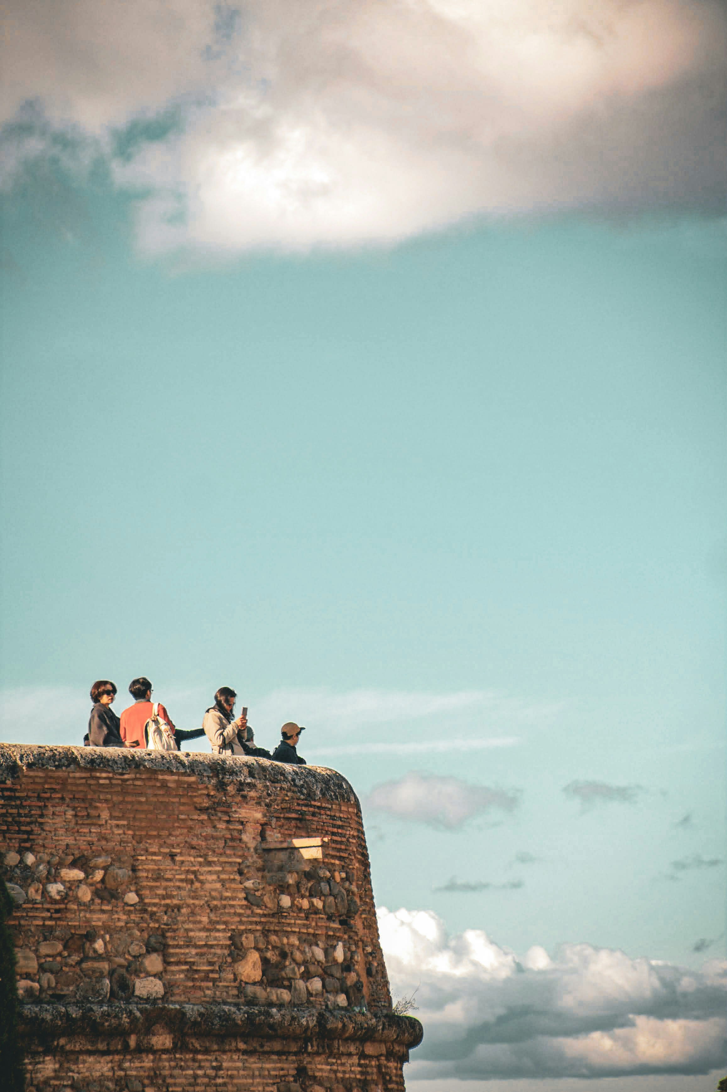 People sitting on a brick wall under a cloudy sky.