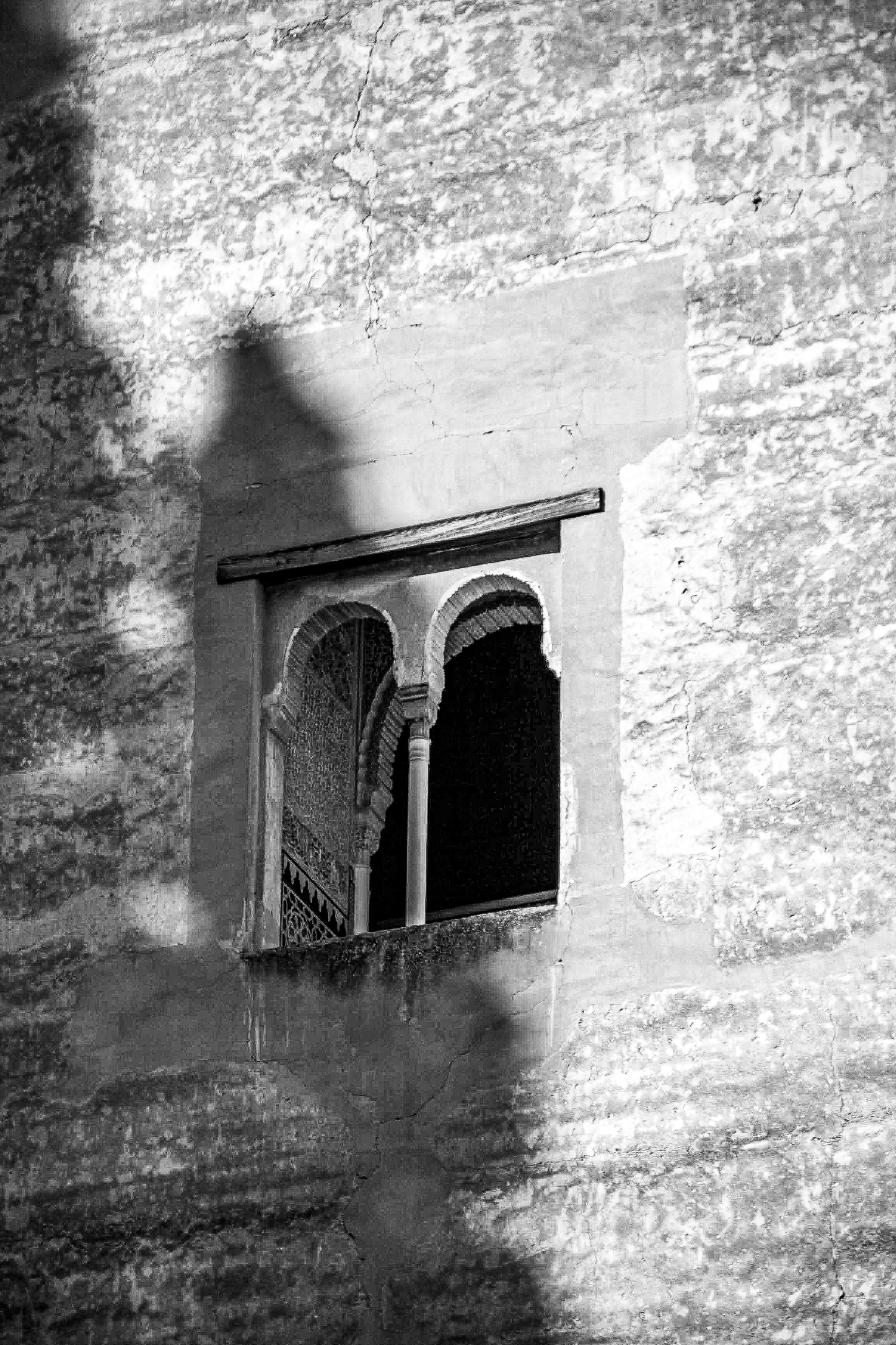 Arched window with ornate details and shadow on textured wall.