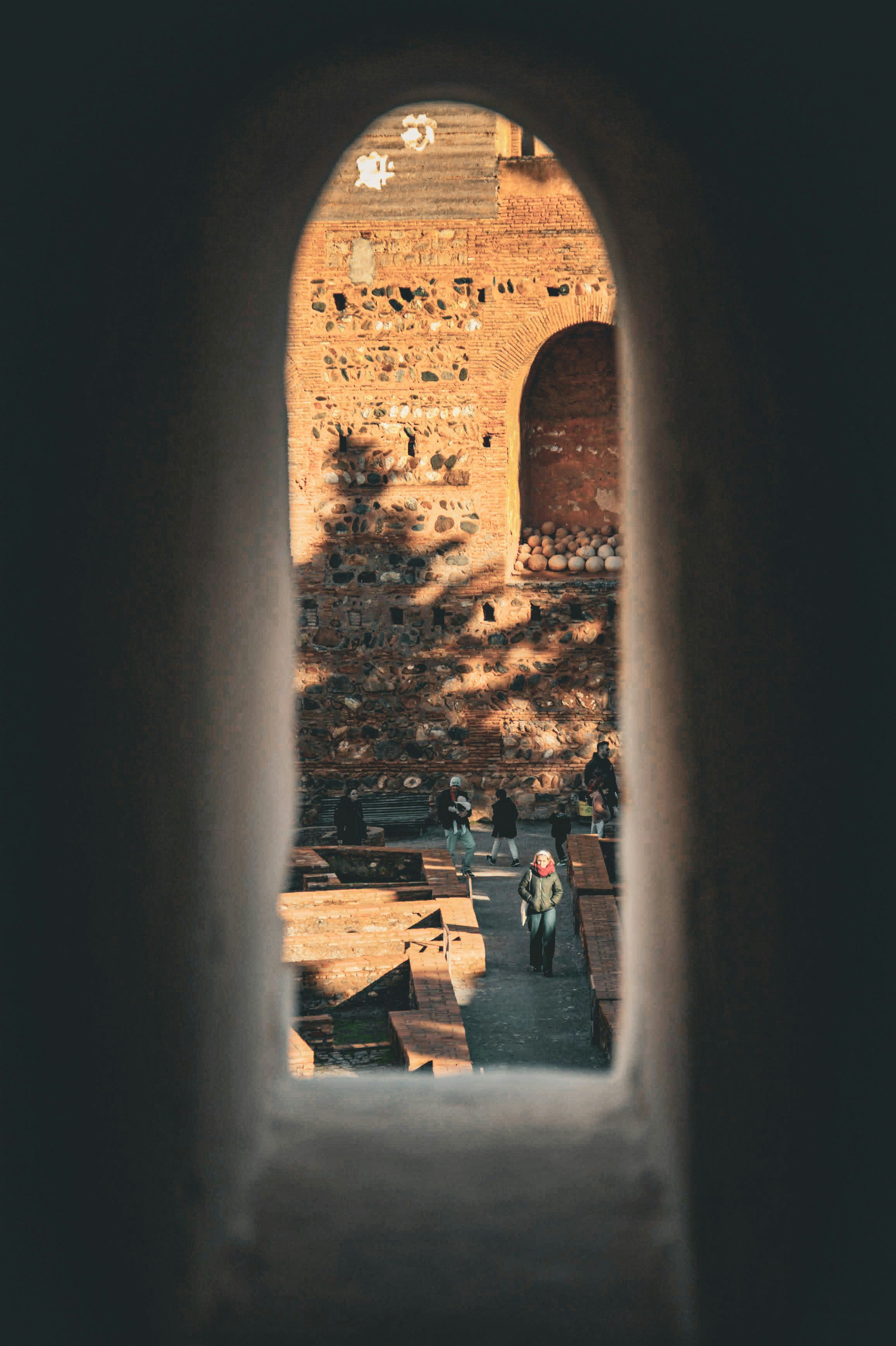 People walking near ancient brick ruins with tree shadows.