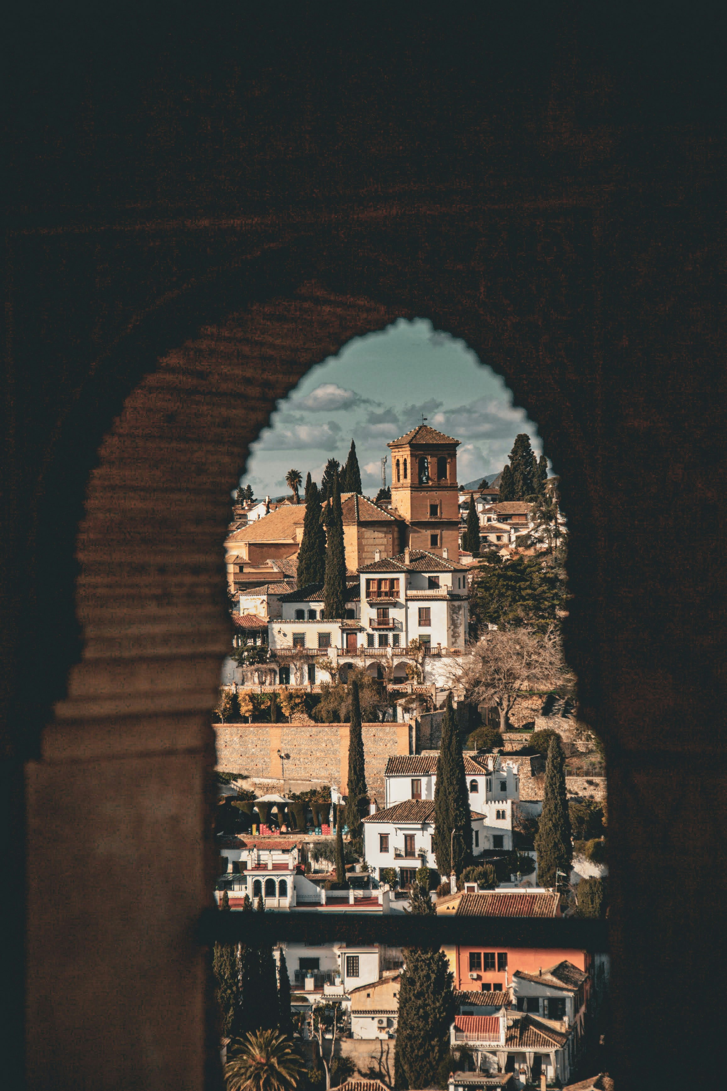 View of white buildings and cypress trees through archway.