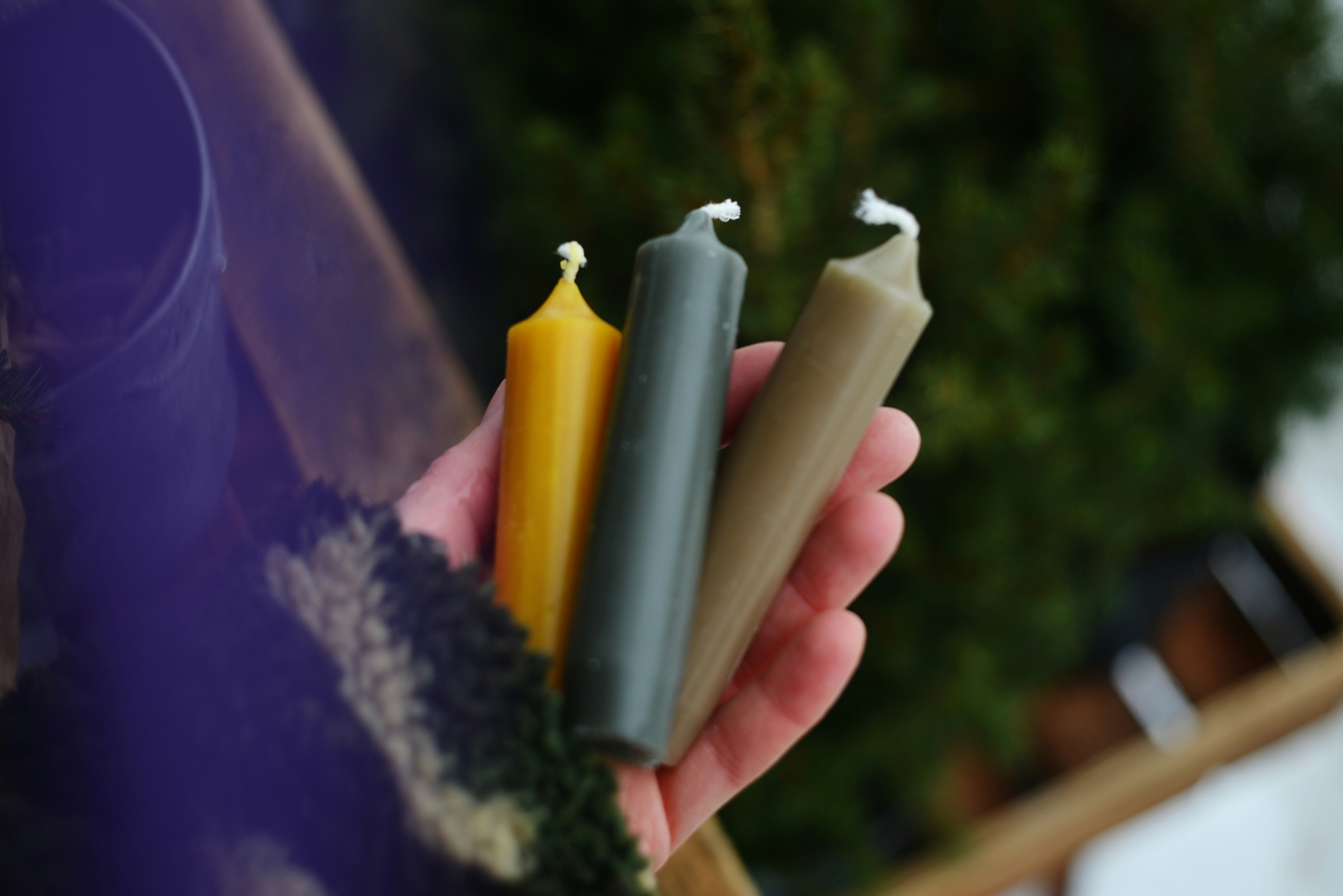 Three unlit candles held in a hand
