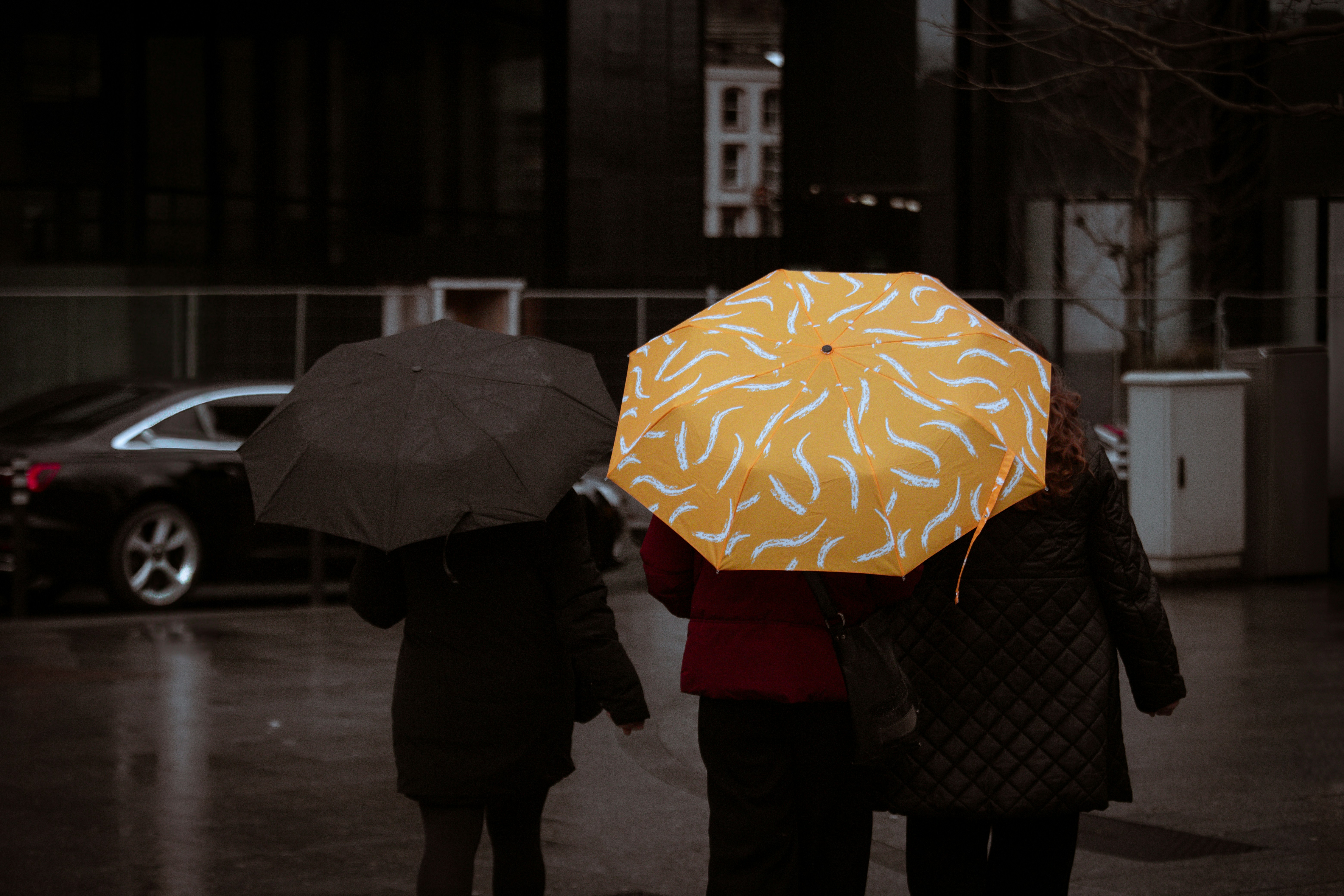Three people walk in the rain under umbrellas.