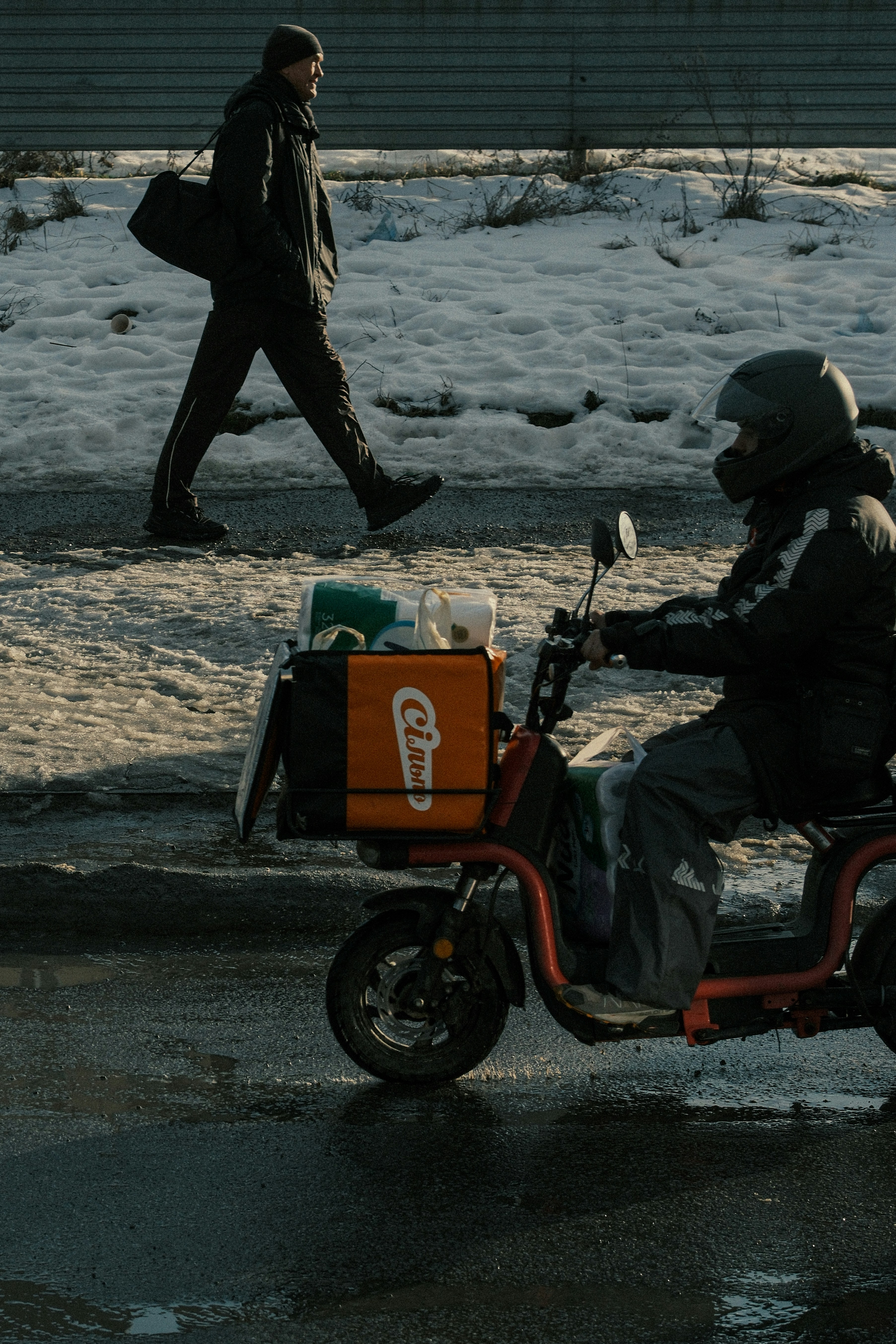 Delivery person on scooter passes pedestrian on snowy street