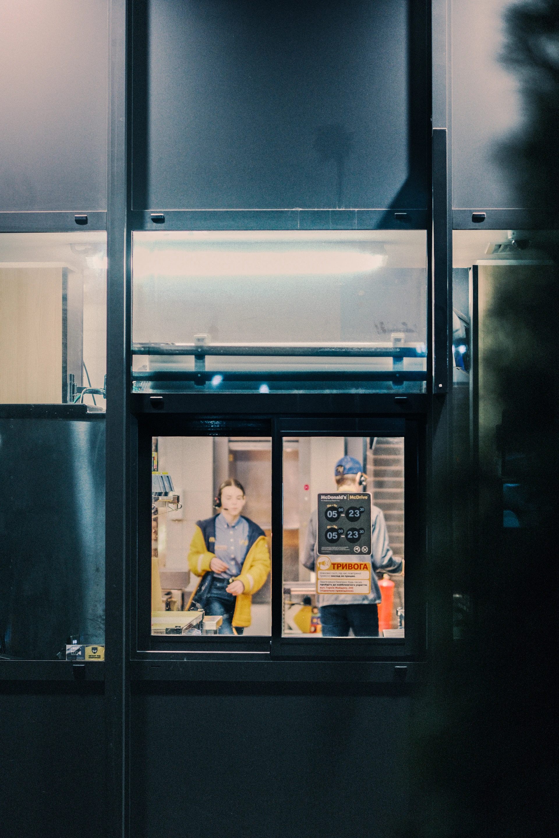 Two men working behind a window at night.