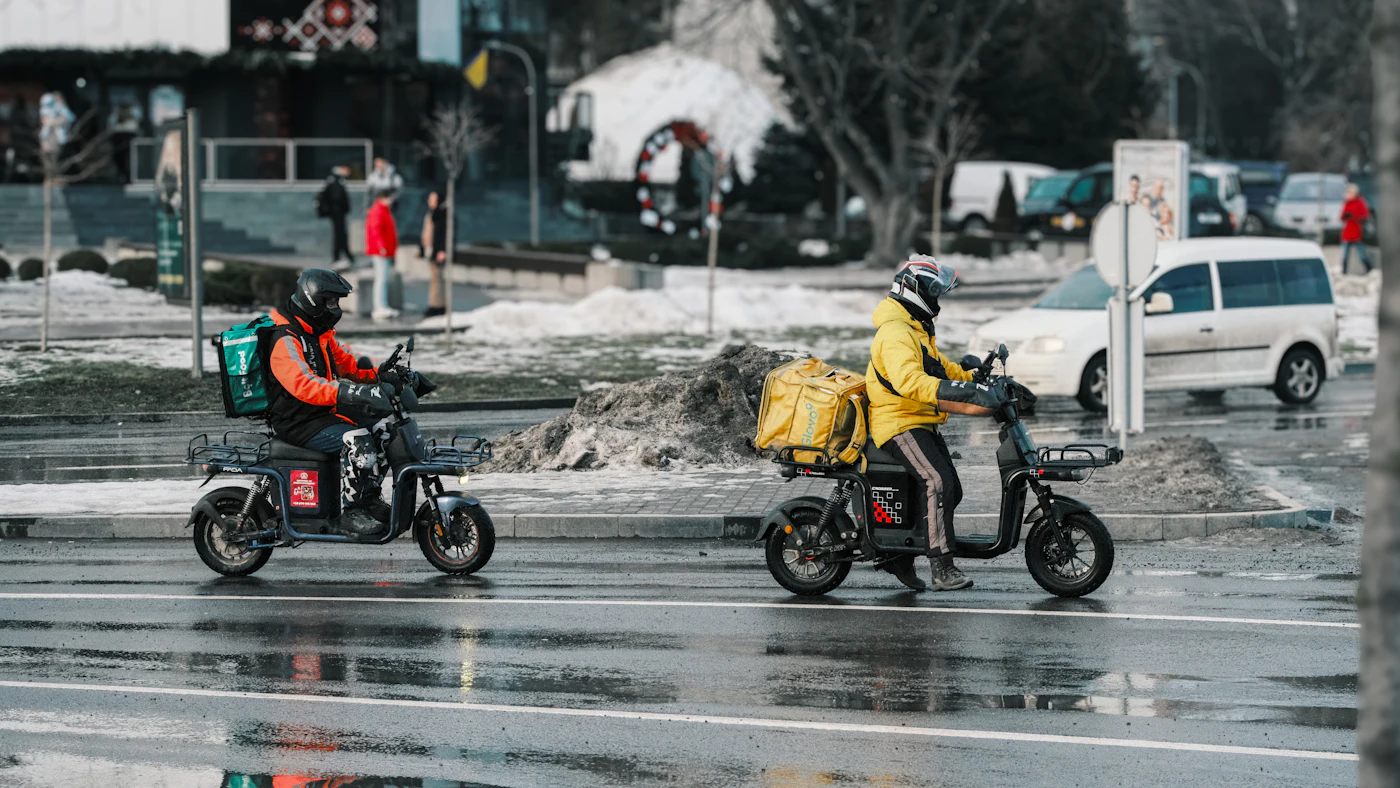 Deux livreurs de repas à scooter avec sacs de livraison sur une rue mouillée