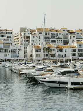 Sailboats and yachts docked in a marina with white buildings.