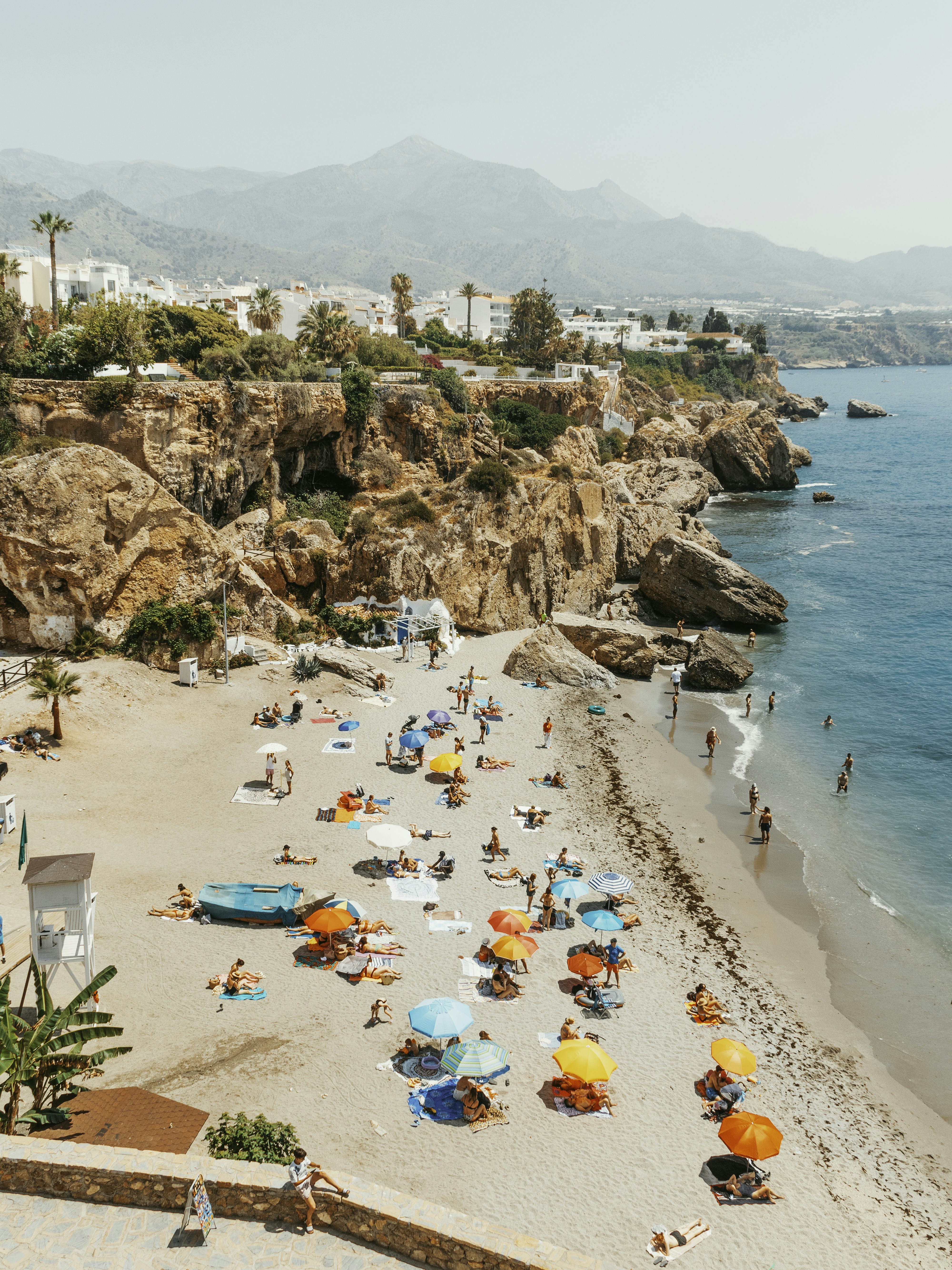 Crowded beach with colorful umbrellas and rocky cliffs