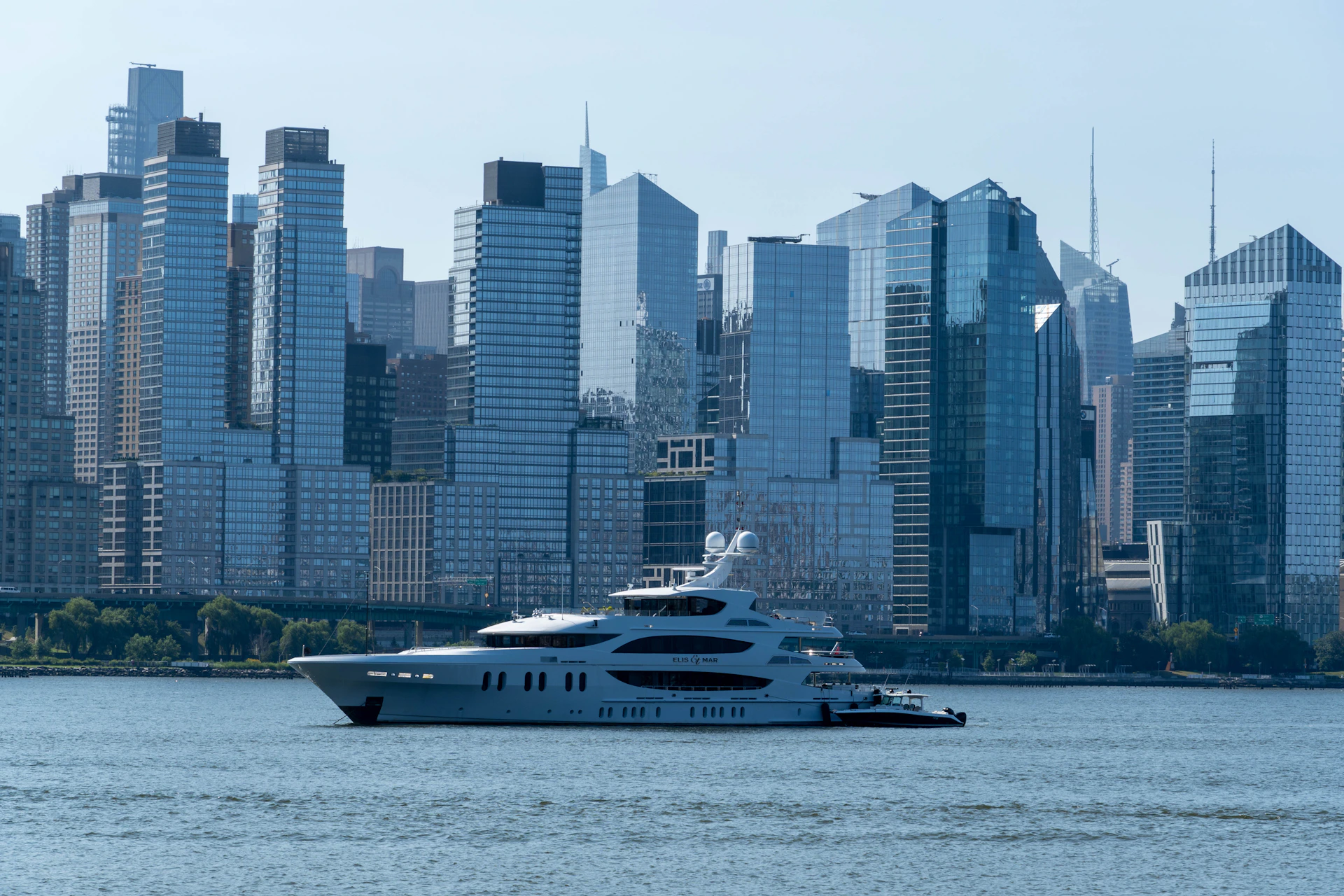 Large white yacht sails on water with city skyline.