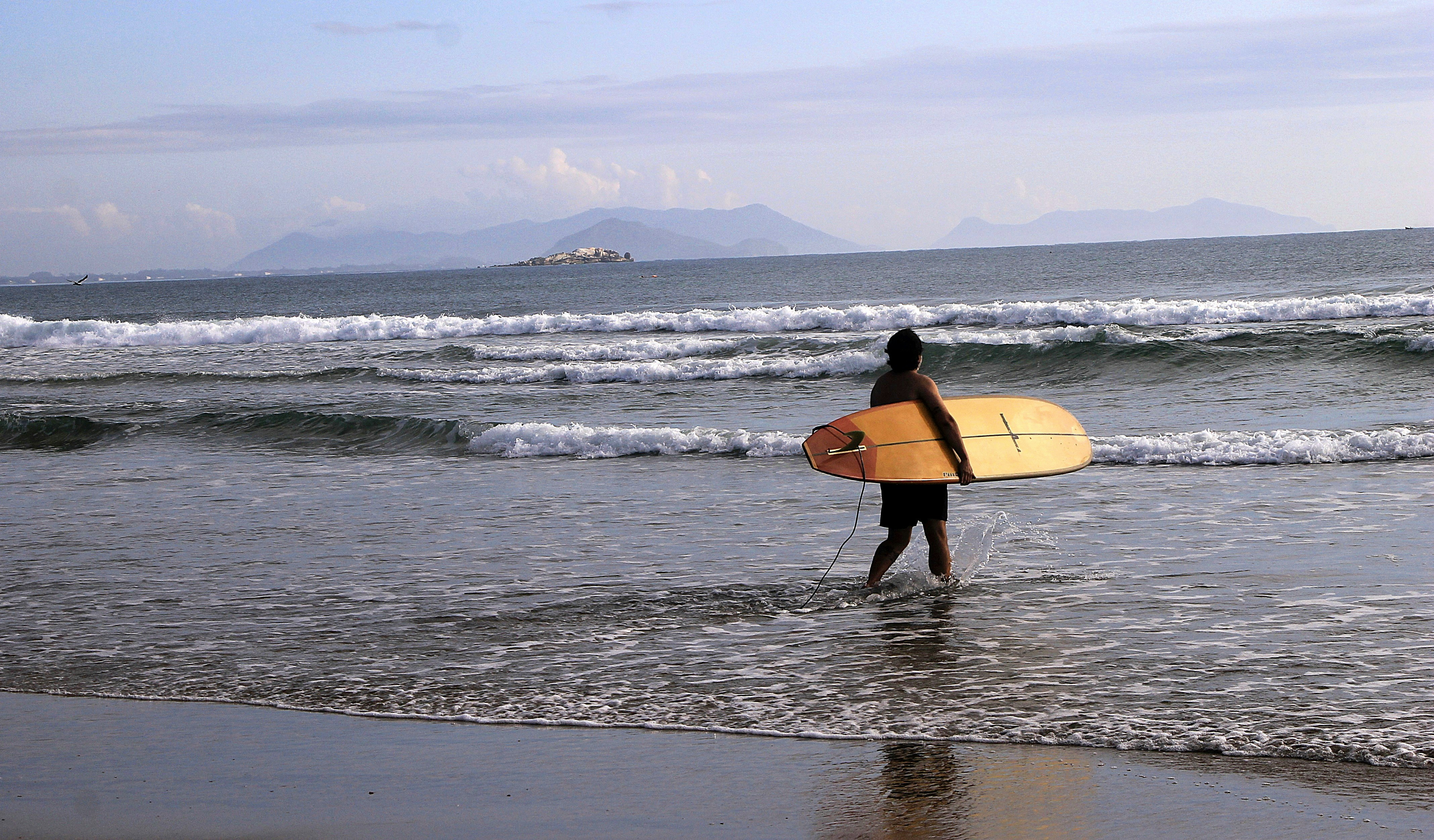 Pessoa entrando no oceano com uma prancha de surfe