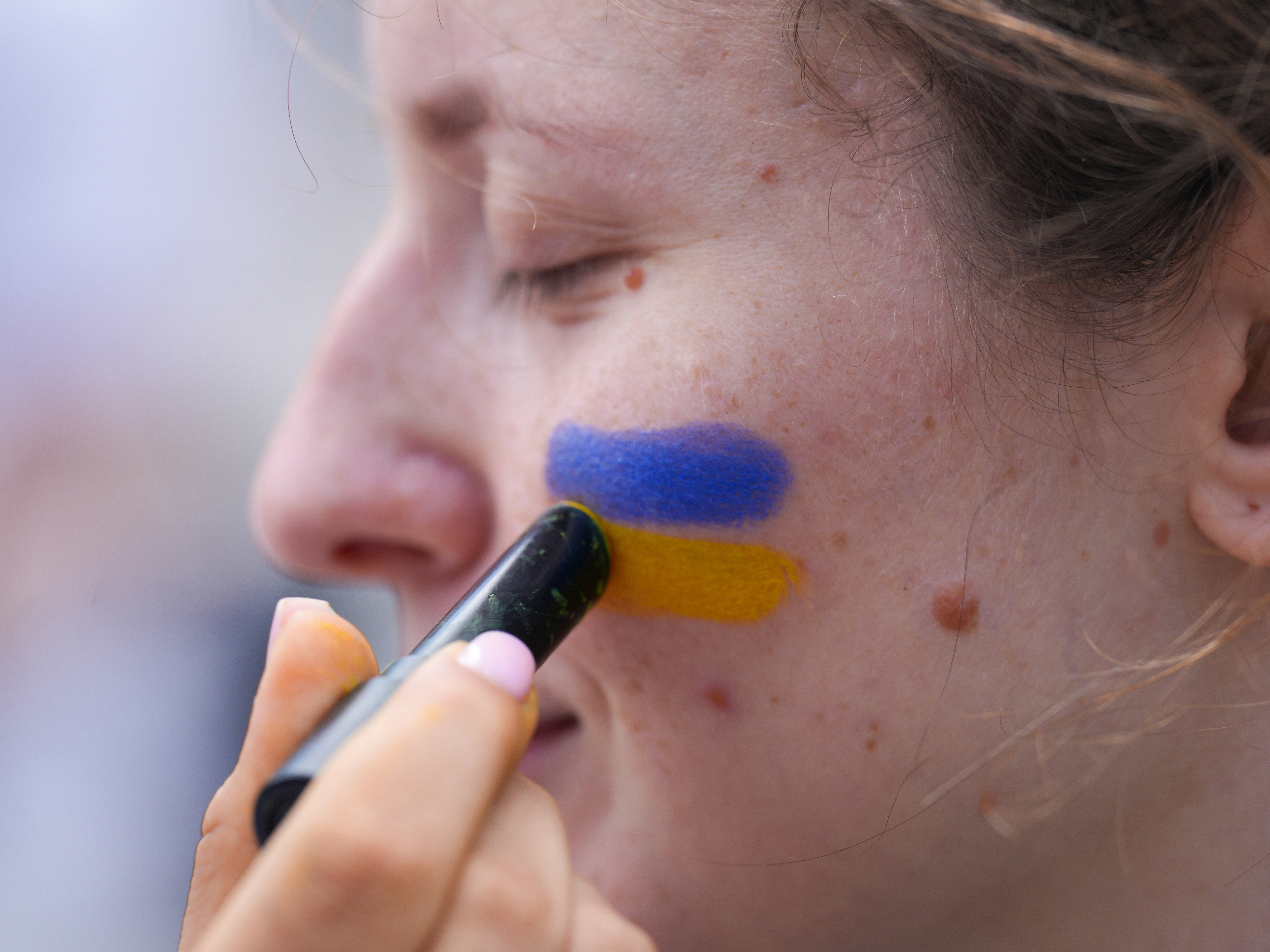 A person applies blue and yellow face paint.