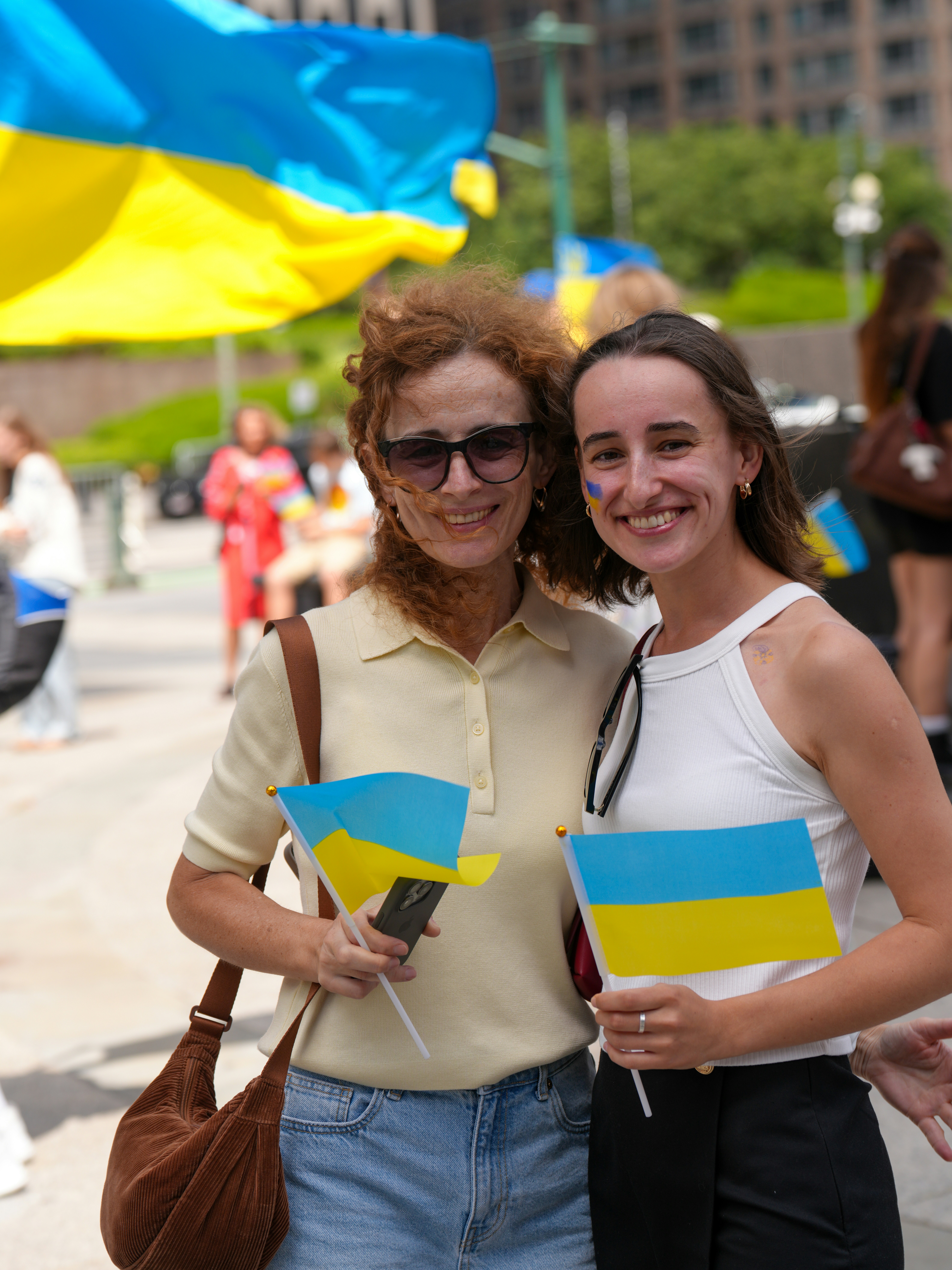 Two smiling women hold ukrainian flags.