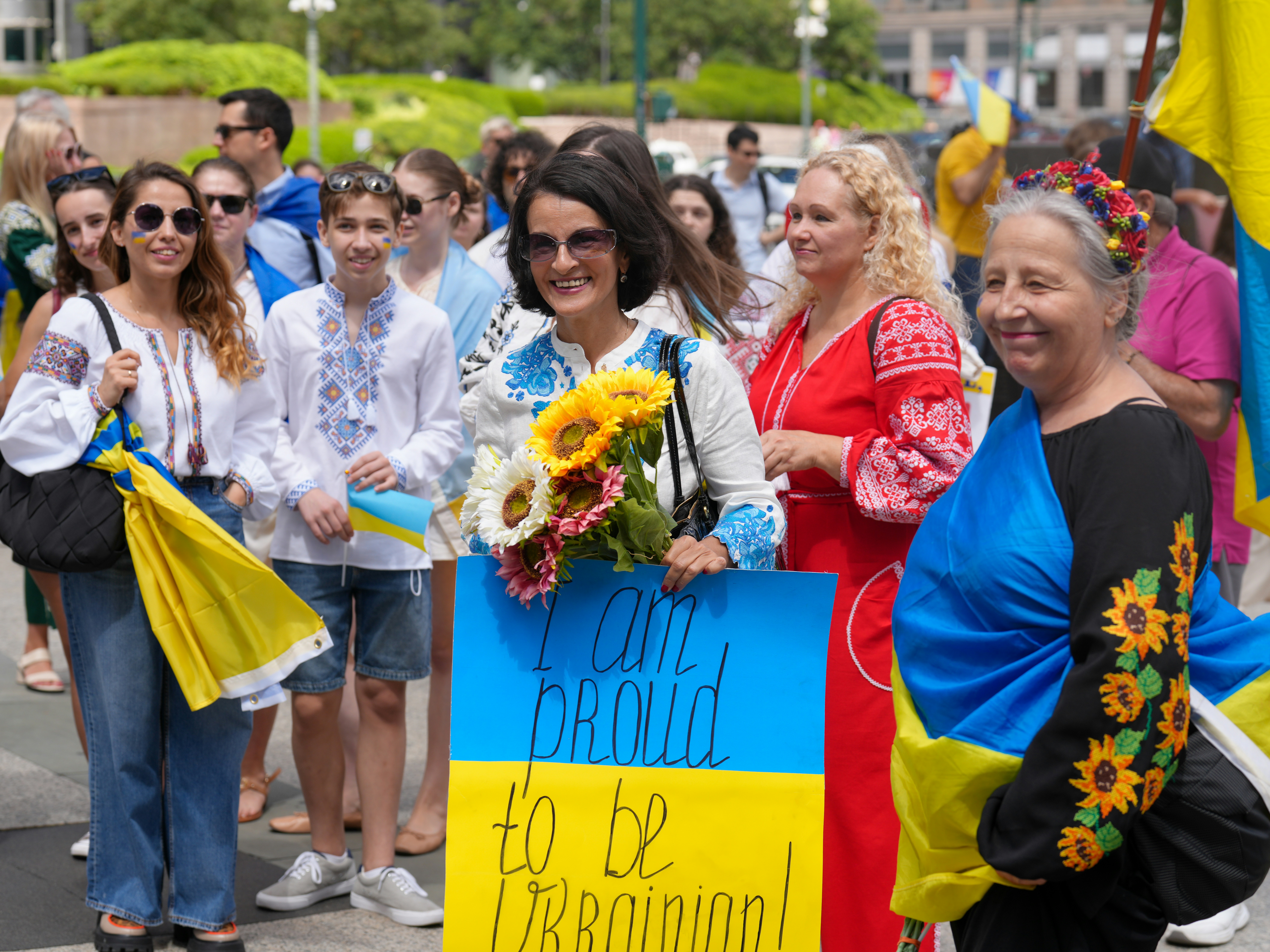 People in traditional ukrainian clothing holding sunflowers and waving flags.