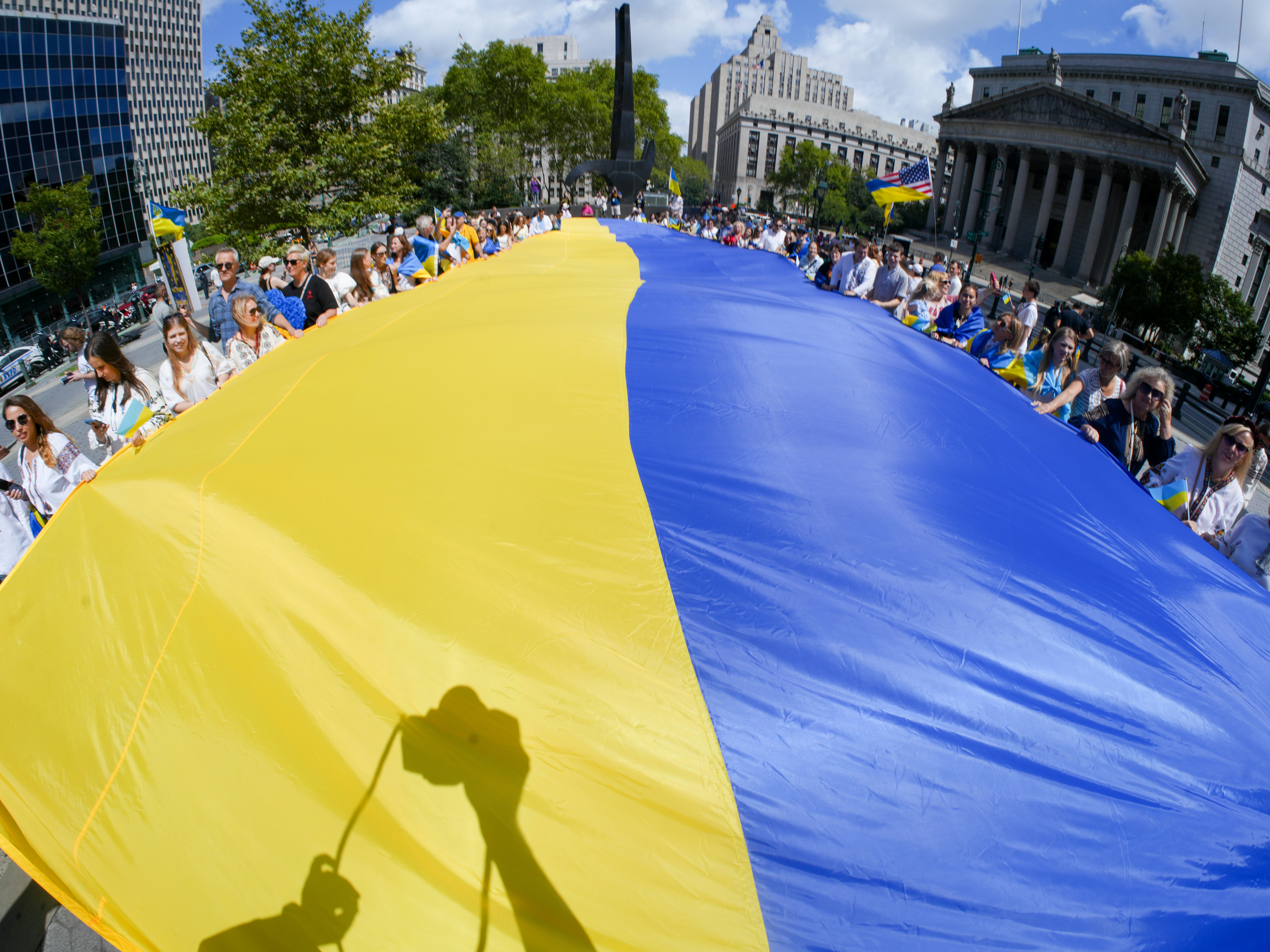 People hold a large ukrainian flag in a city square.