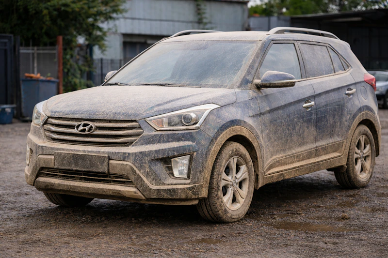 Dark SUV covered in road grime with mud-caked wheels and dulled paint before detailing