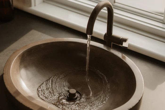 Water running from a dark tap into a hammered bronze basin