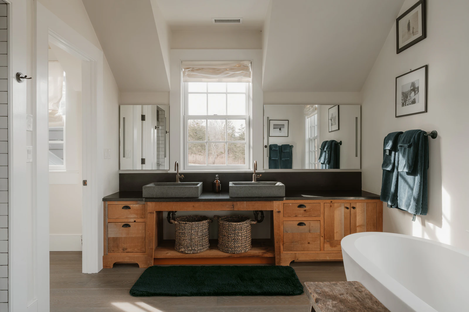 Bright bathroom with a timber double vanity, two vessel sinks, large mirrors, framed artwork, a freestanding bathtub and natural light.