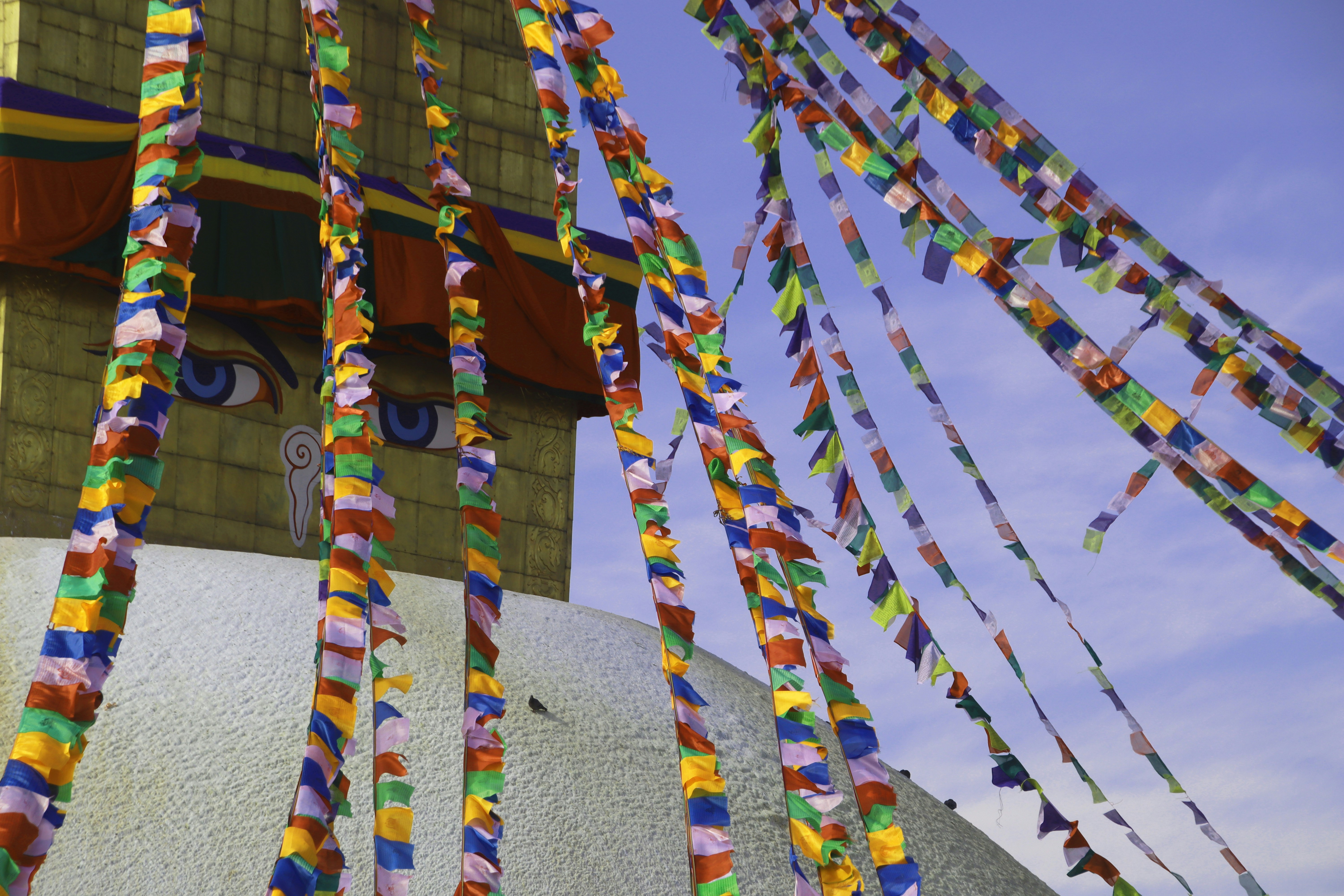 Colorful prayer flags flutter around a stupa with eyes.