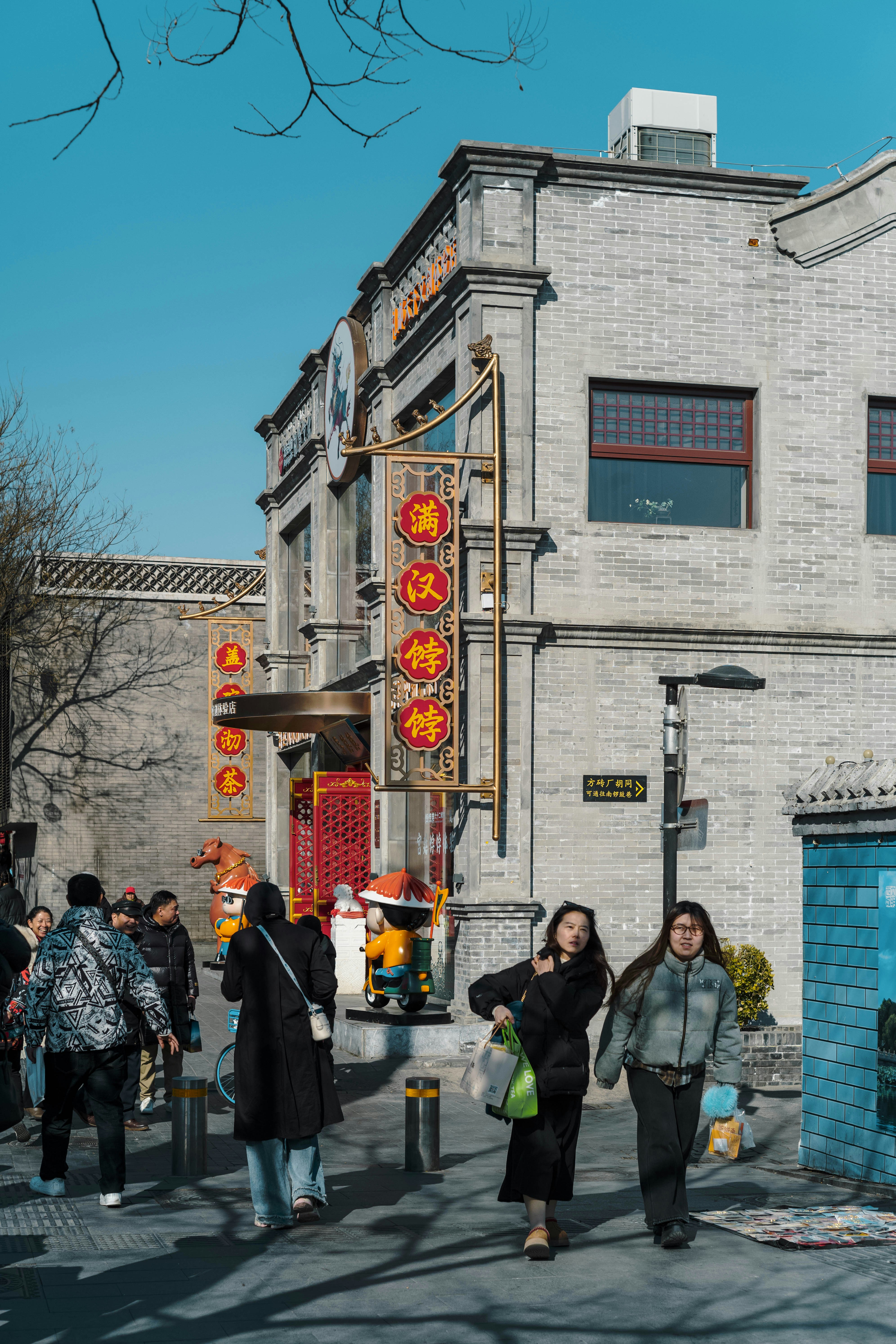 People walk past a traditional building with red lanterns.