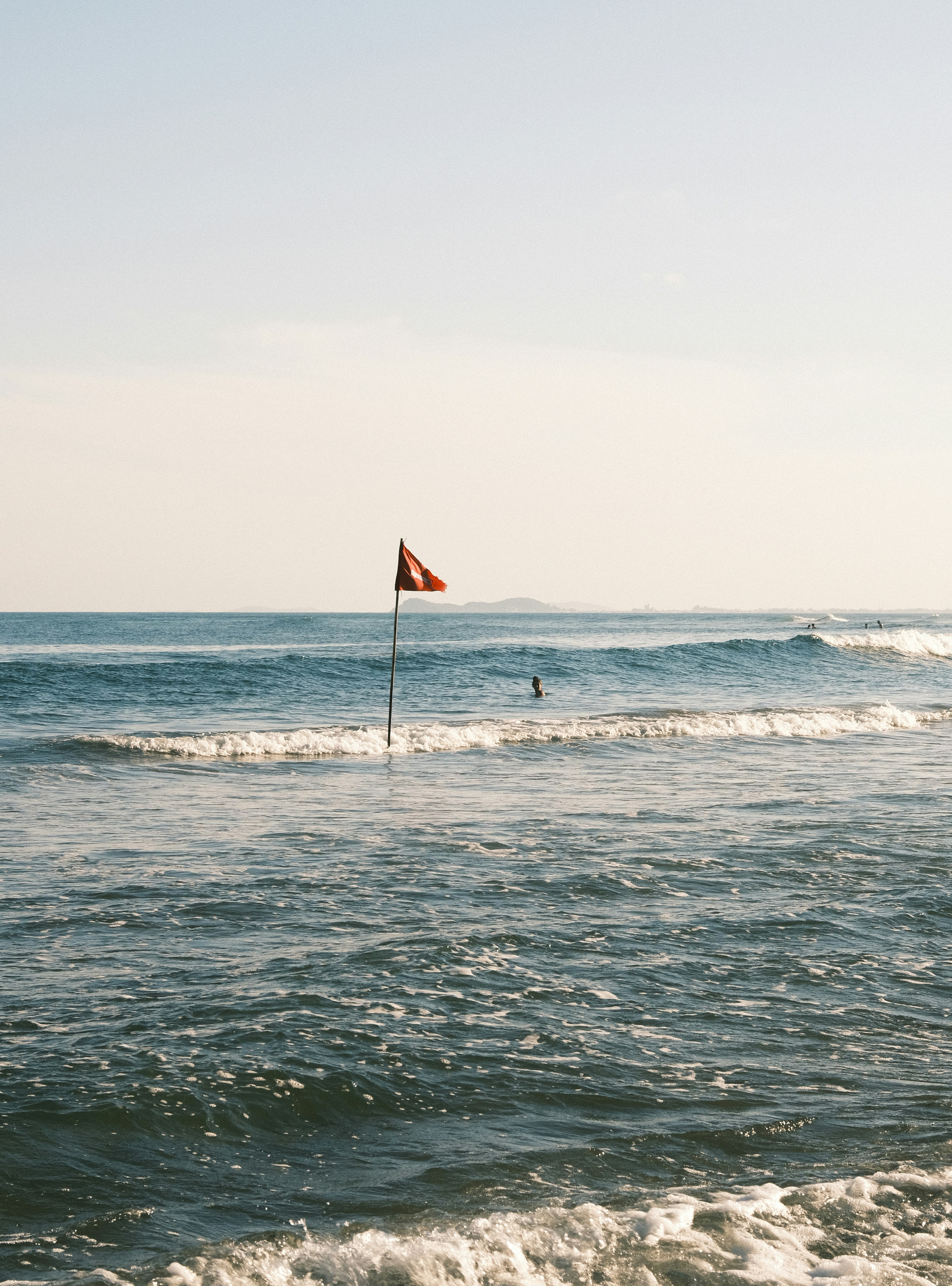 A red flag stands on a pole in the ocean.
