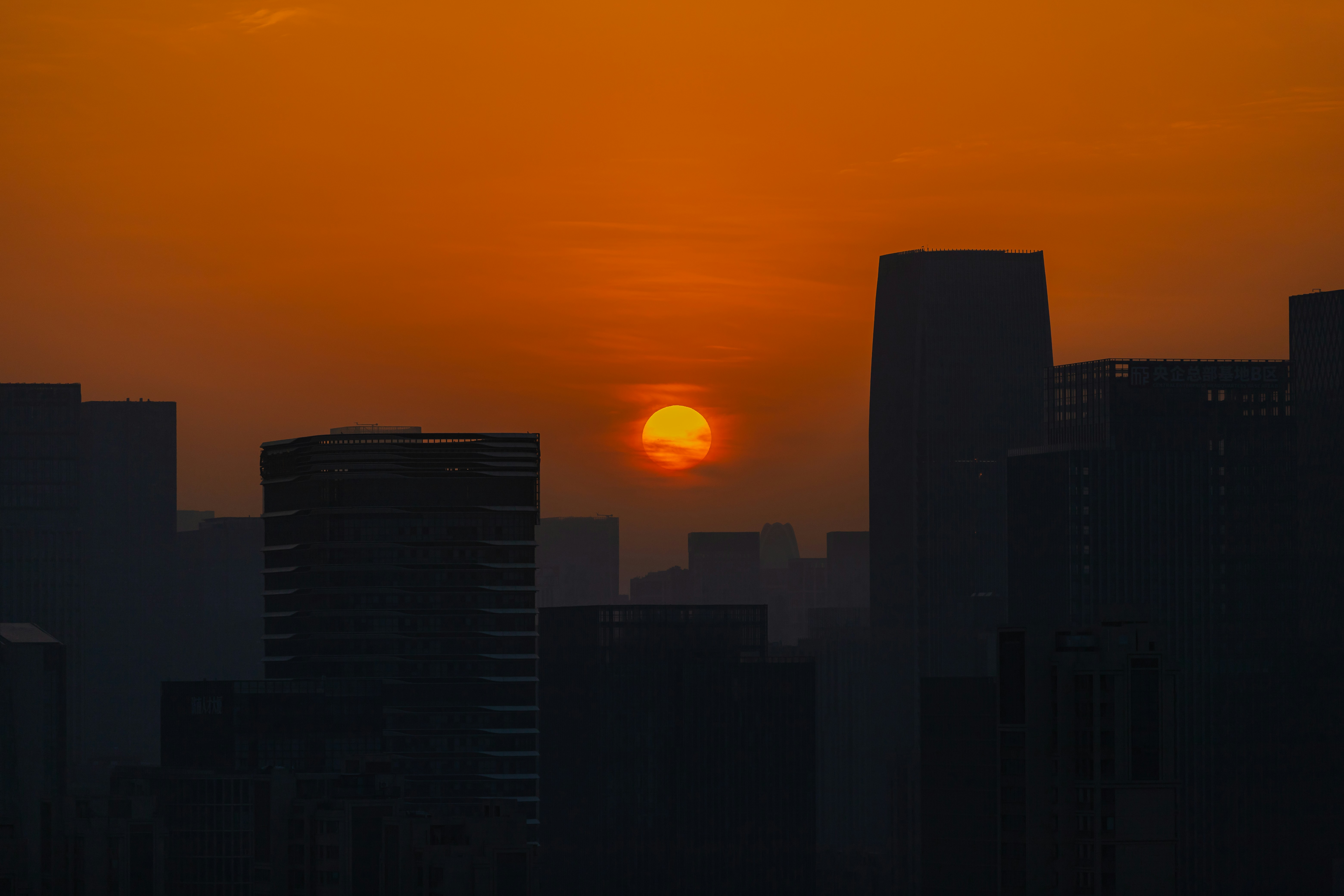 Sunrise over a hazy cityscape with silhouetted buildings.