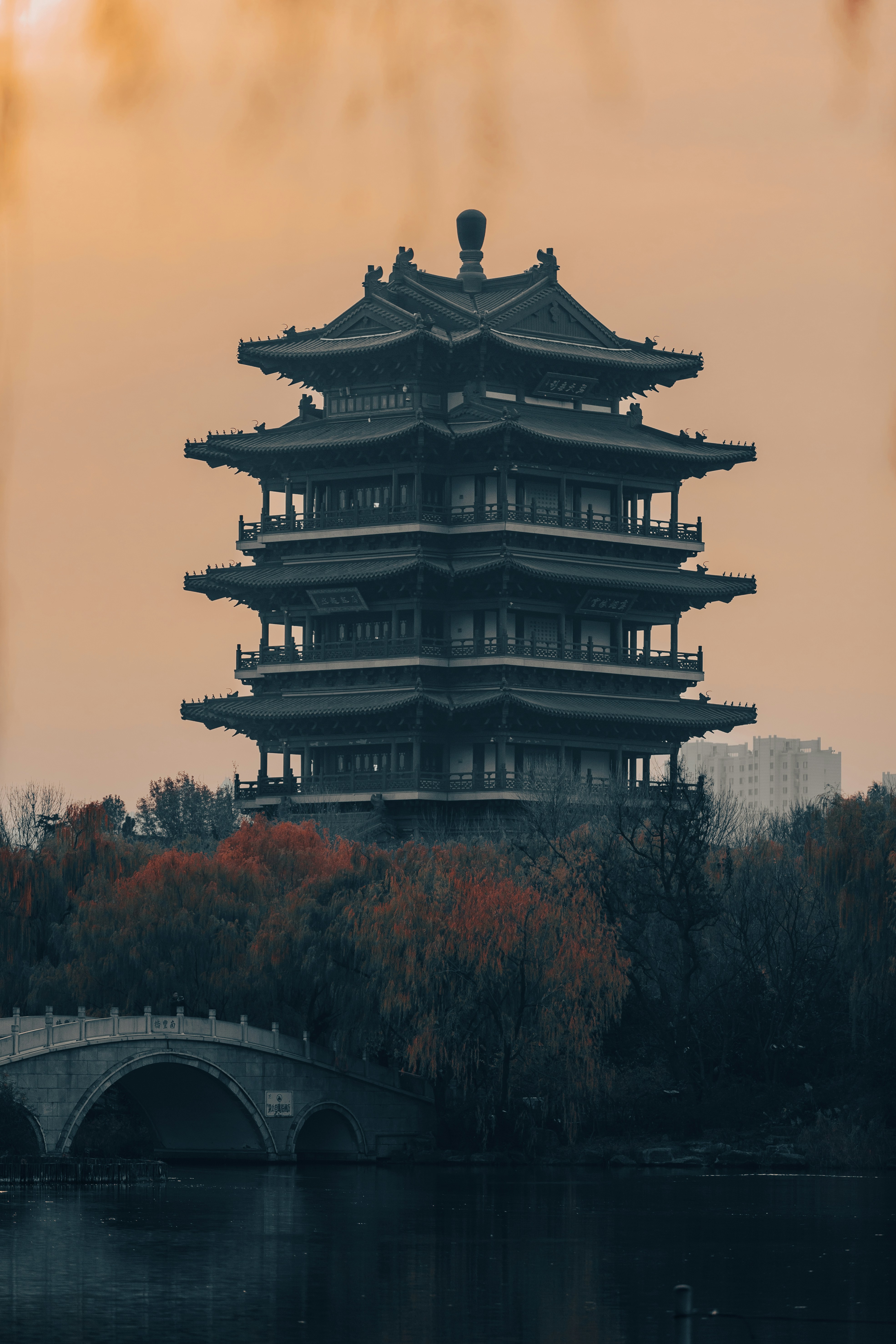 伝統的な塔の建築で、アーチ型の橋と秋の木々が特徴です。