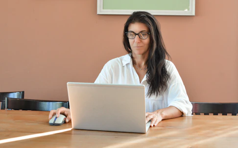 A woman wearing glasses works on a laptop.