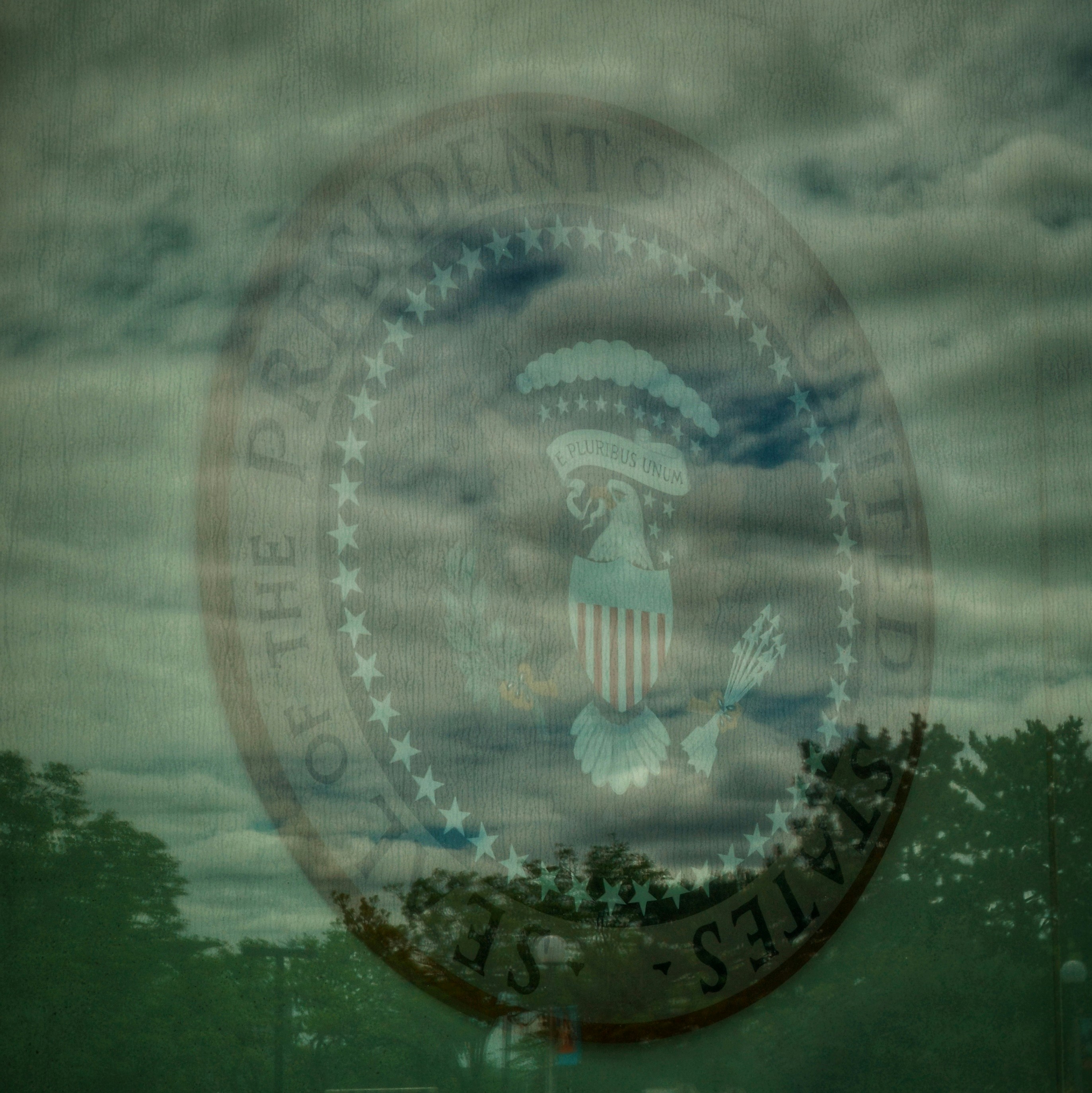 Presidential seal superimposed on cloudy sky and trees