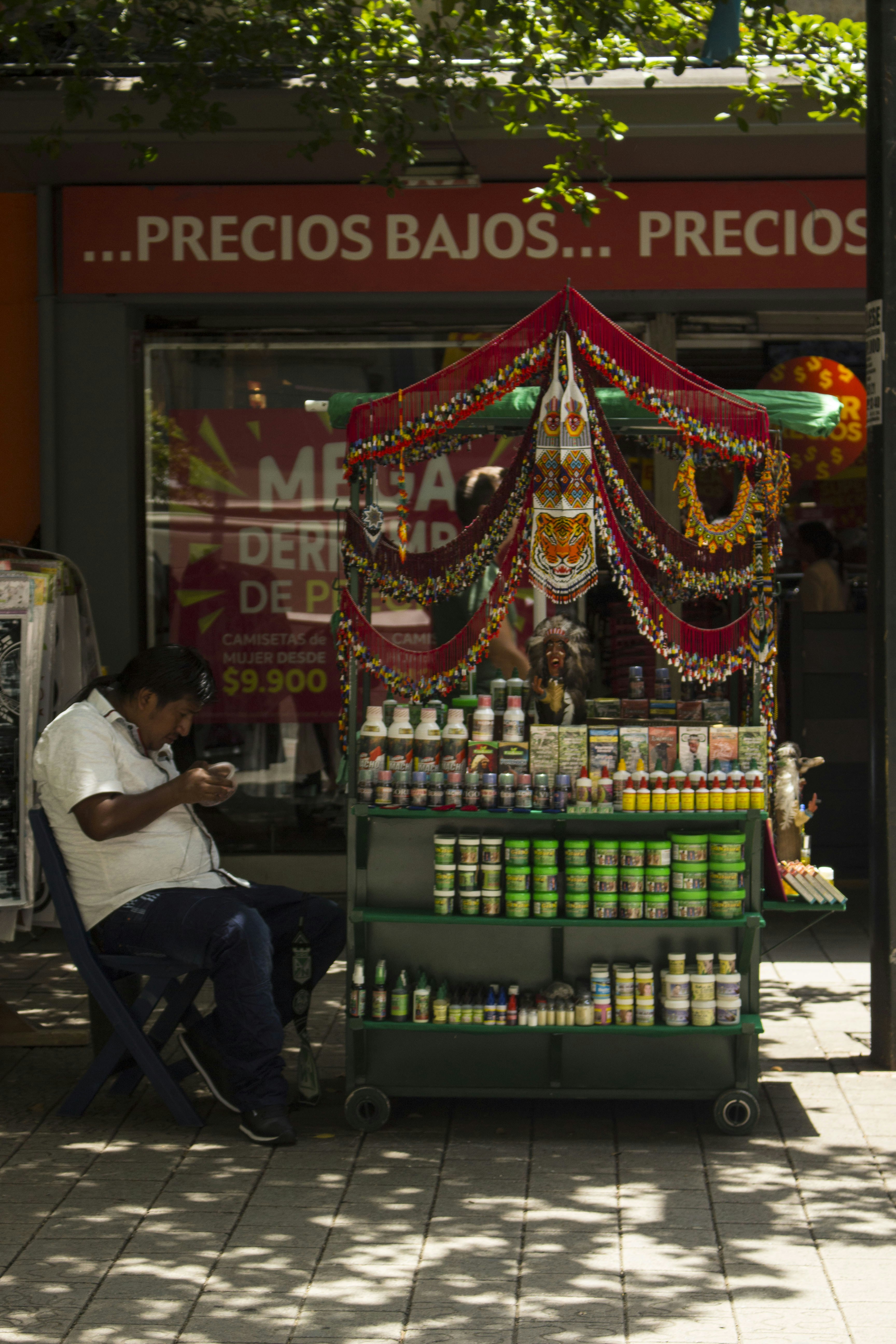 Man sitting by a colorful street vendor cart.